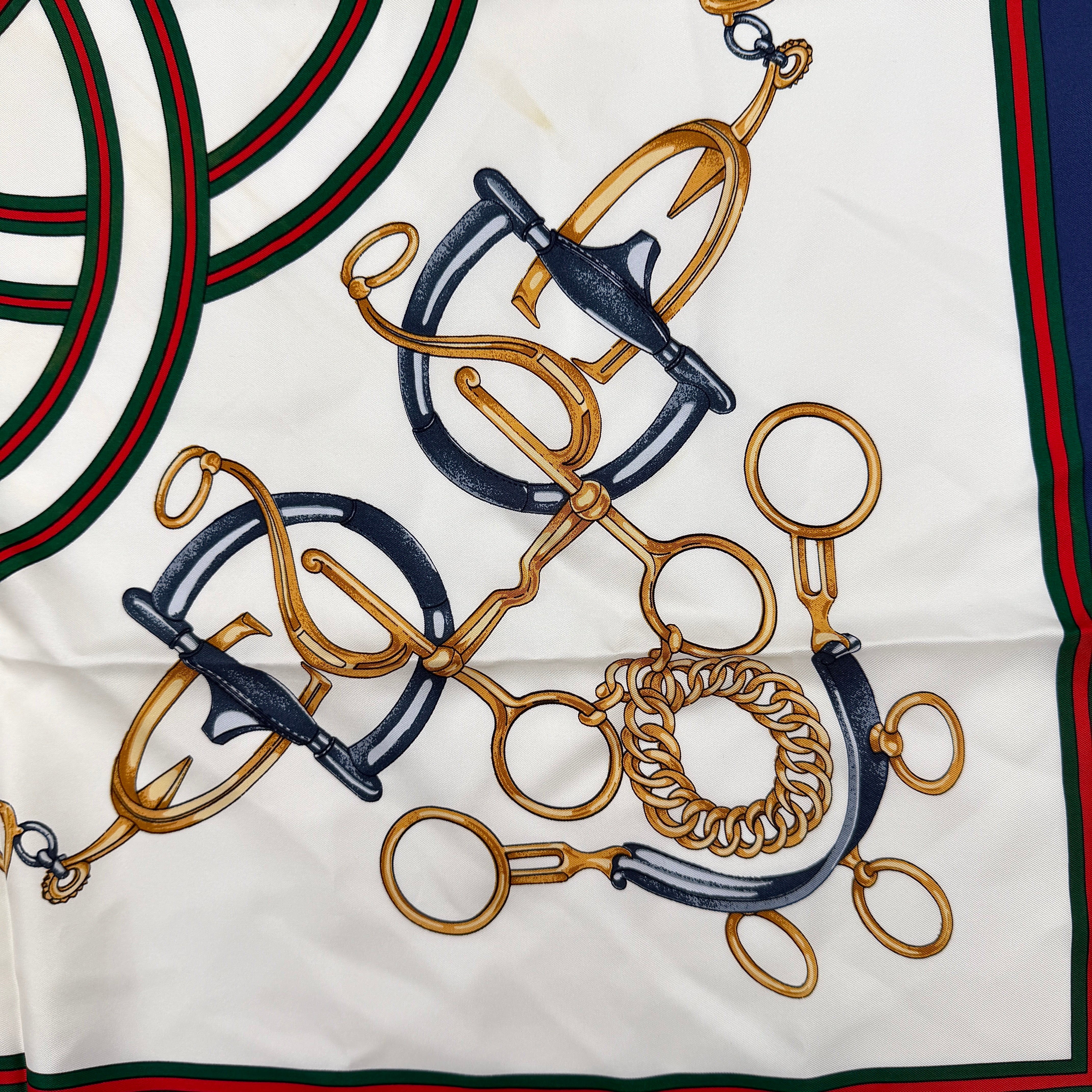 Gucci silk scarf with equestrian horsebit print, navy borders, and large GG logo displayed against a white background.