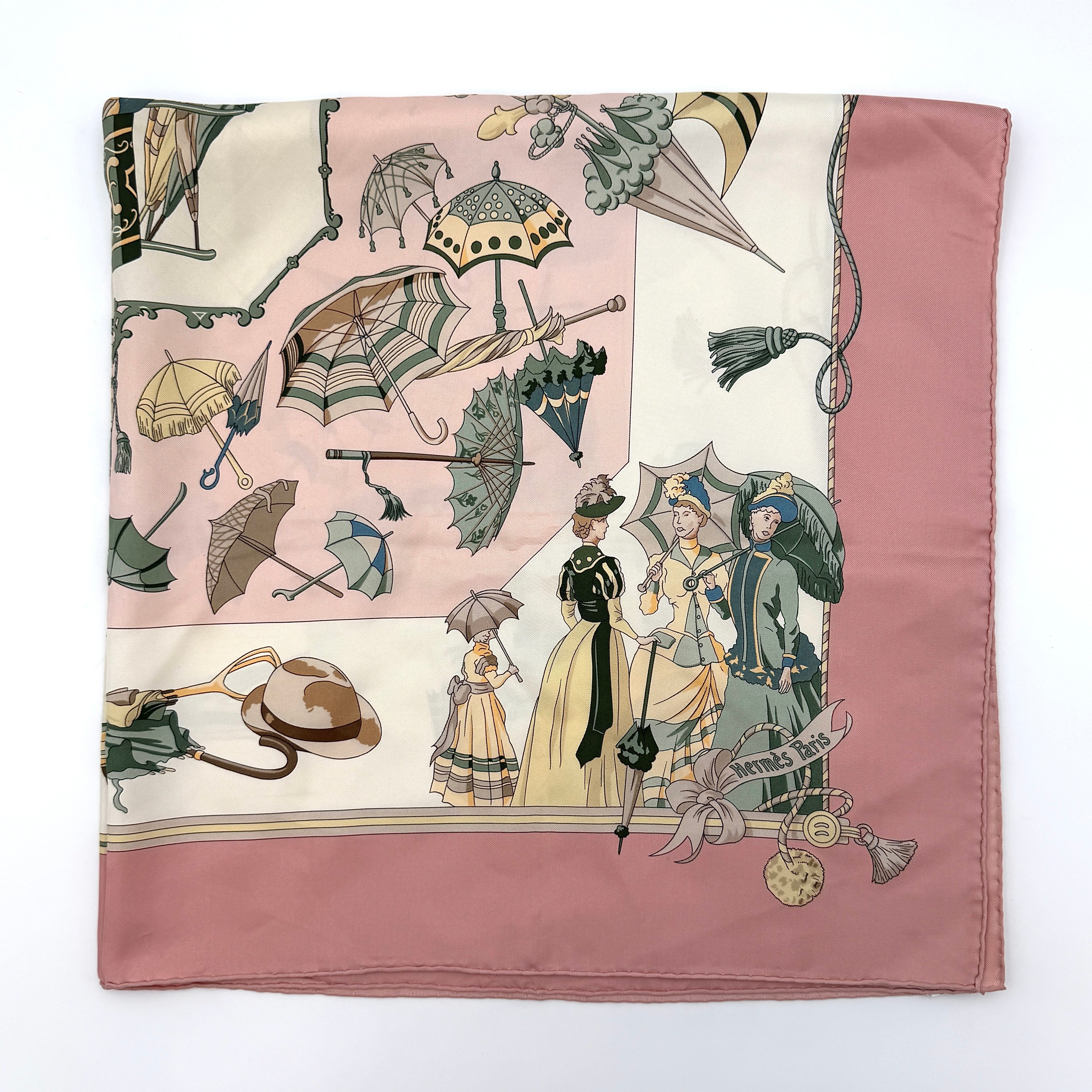 Hermès Ombrelles et Parapluies silk scarf in pink with umbrella print and illustrated figures, gracefully draped to show the intricate design.