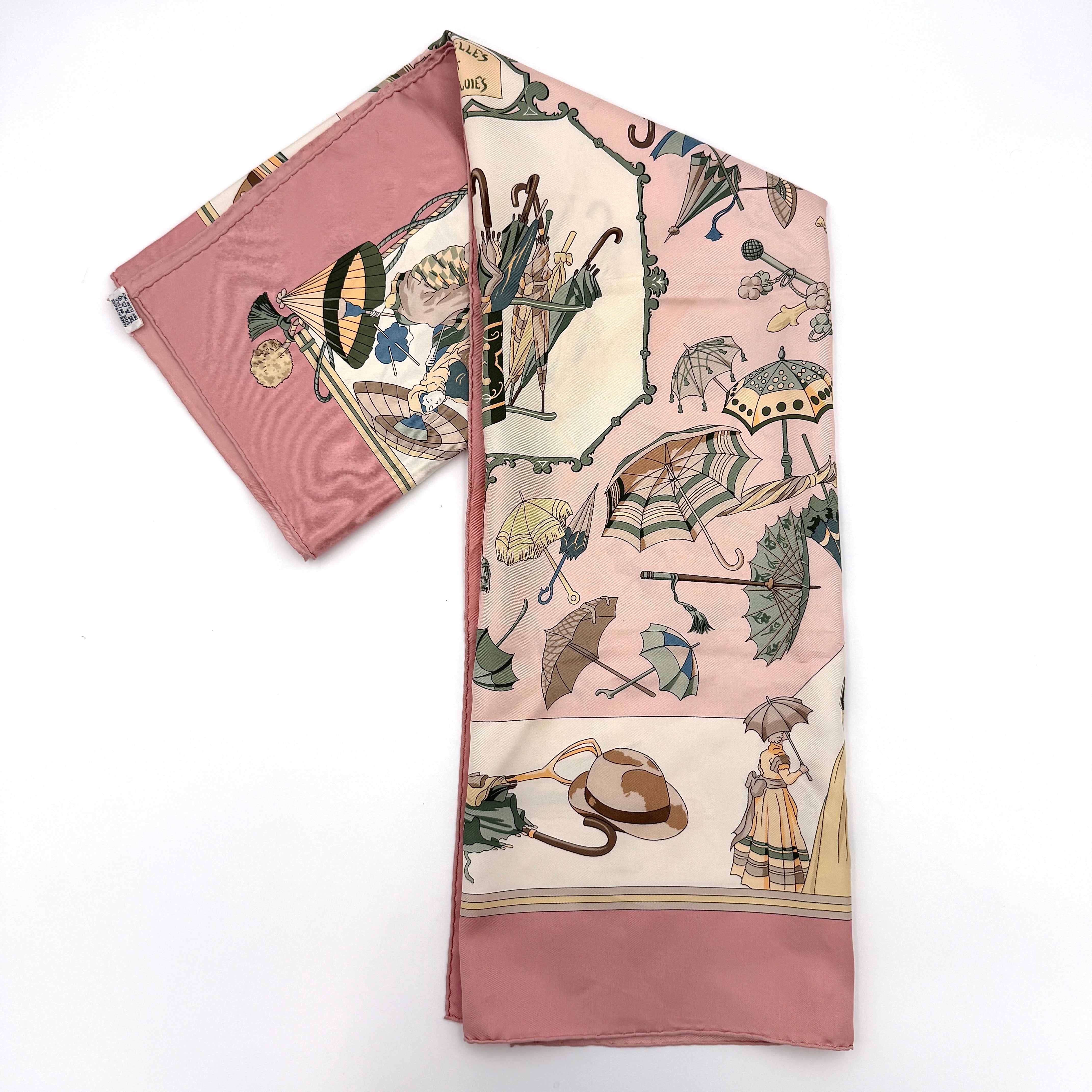 Hermès Ombrelles et Parapluies silk scarf in pink with umbrella print and illustrated figures, gracefully draped to show the intricate design.