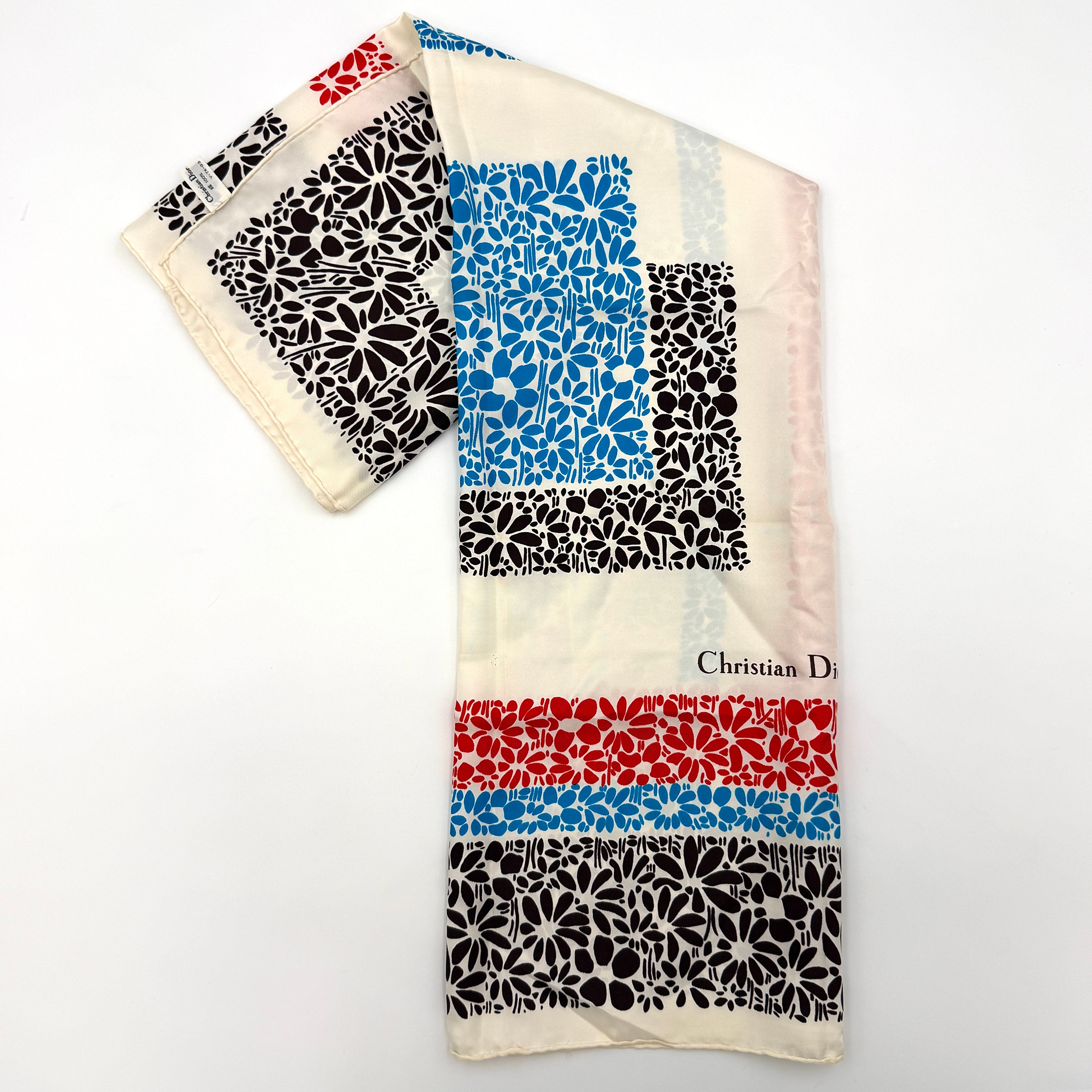 Dior silk scarf featuring a bold multicolor geometric floral pattern in red, blue, black, and ivory with the Christian Dior logo visible at the corner.