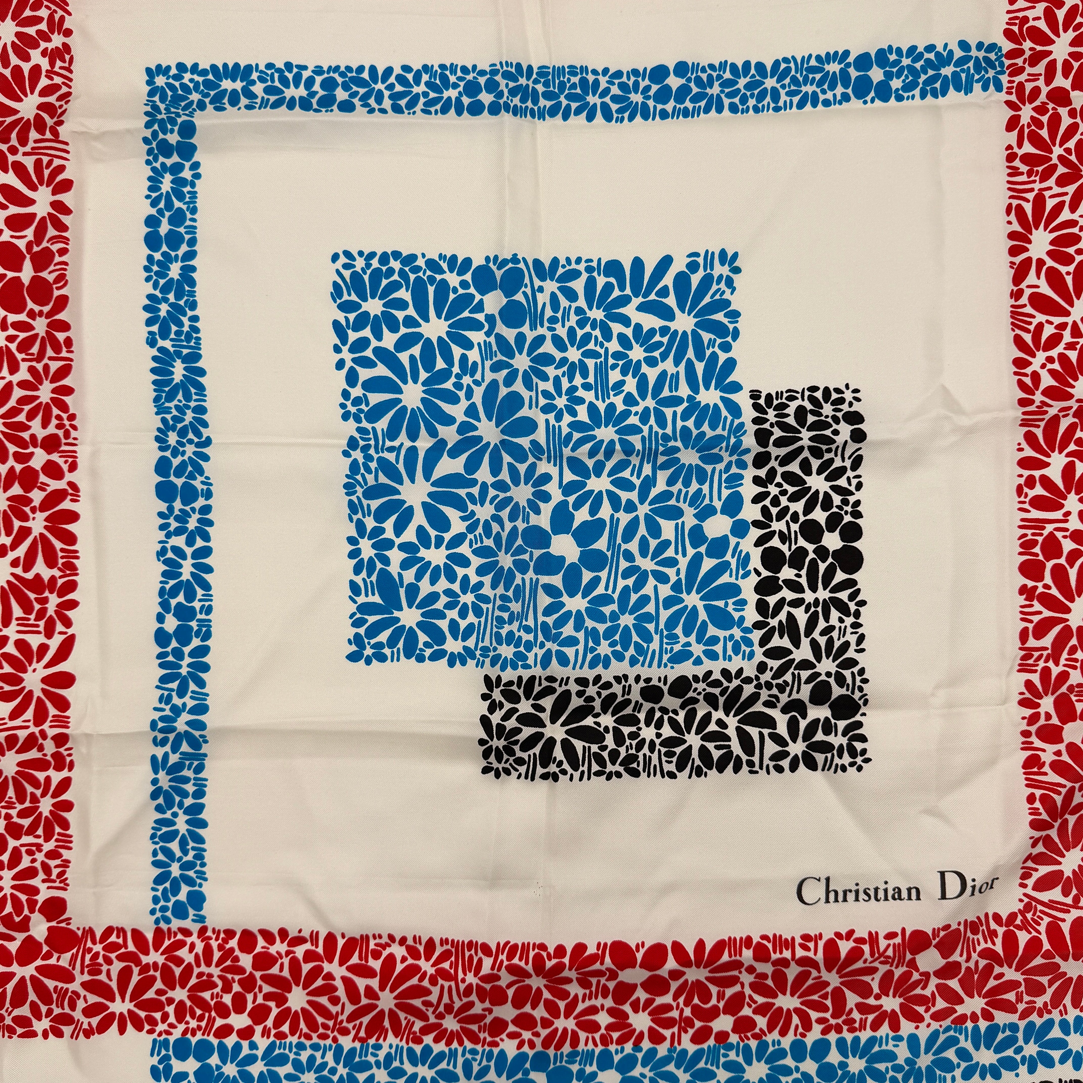 Dior silk scarf featuring a bold multicolor geometric floral pattern in red, blue, black, and ivory with the Christian Dior logo visible at the corner.