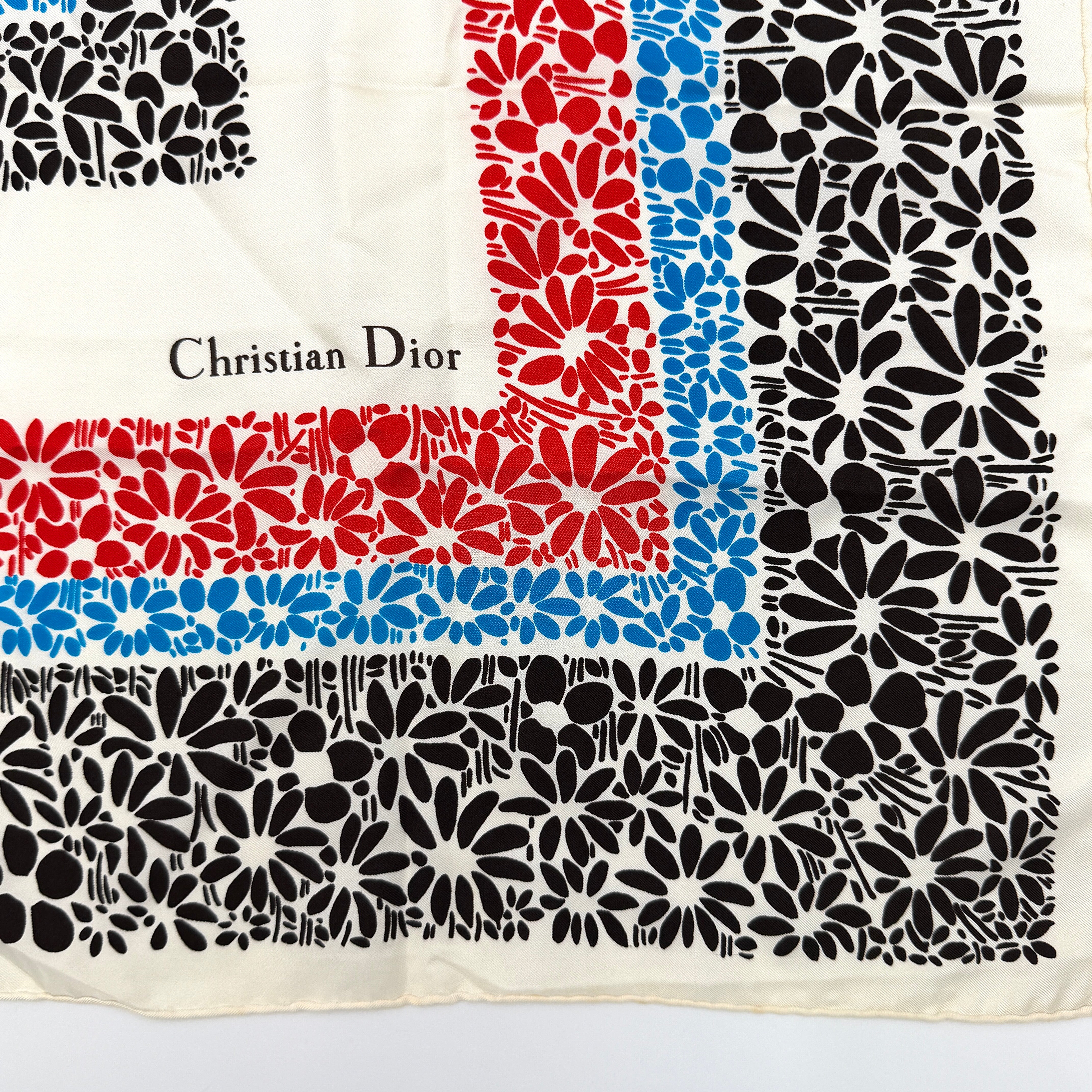 Dior silk scarf featuring a bold multicolor geometric floral pattern in red, blue, black, and ivory with the Christian Dior logo visible at the corner.