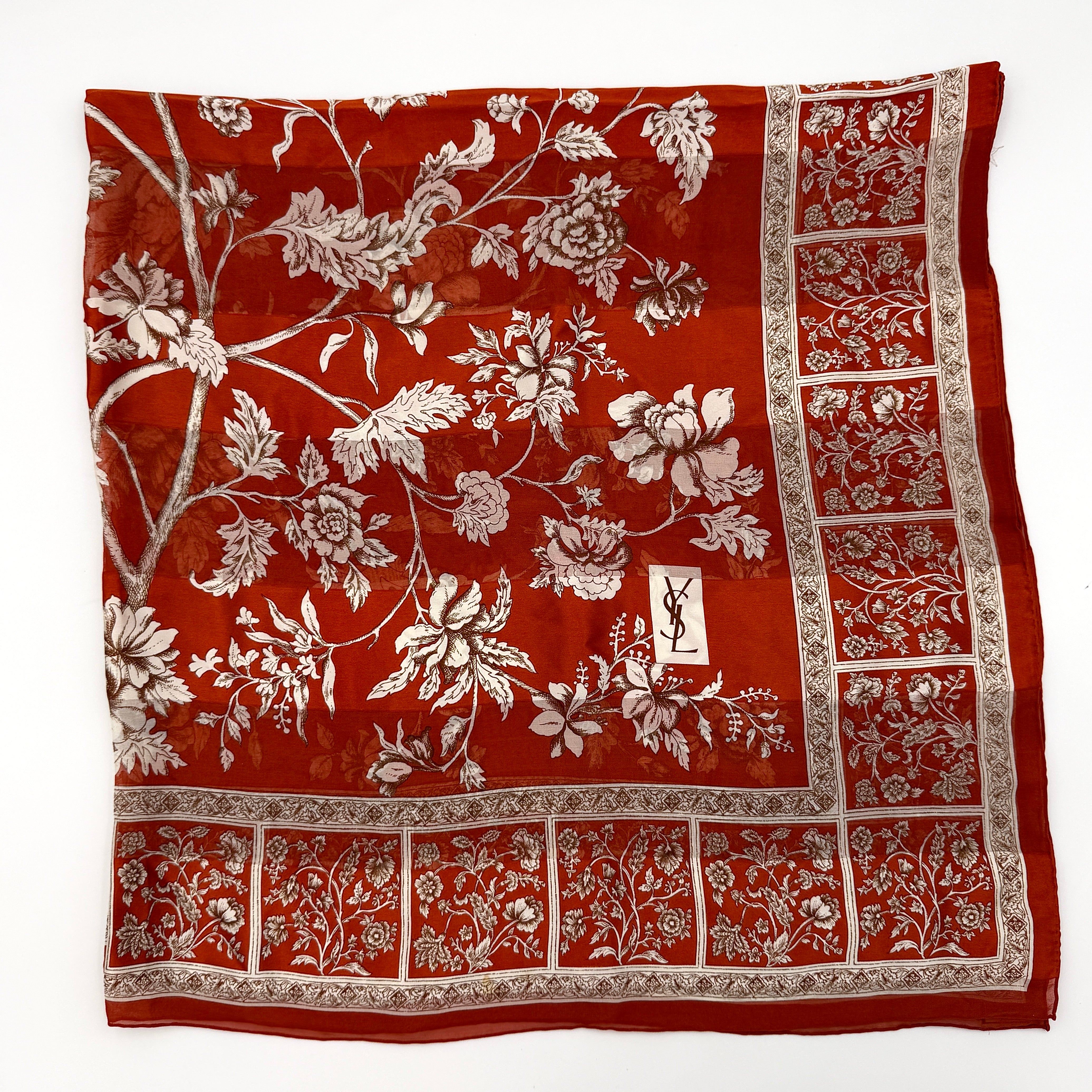Saint Laurent silk scarf in rich red, featuring intricate cream floral designs and ornate borders with the YSL monogram visibly displayed.