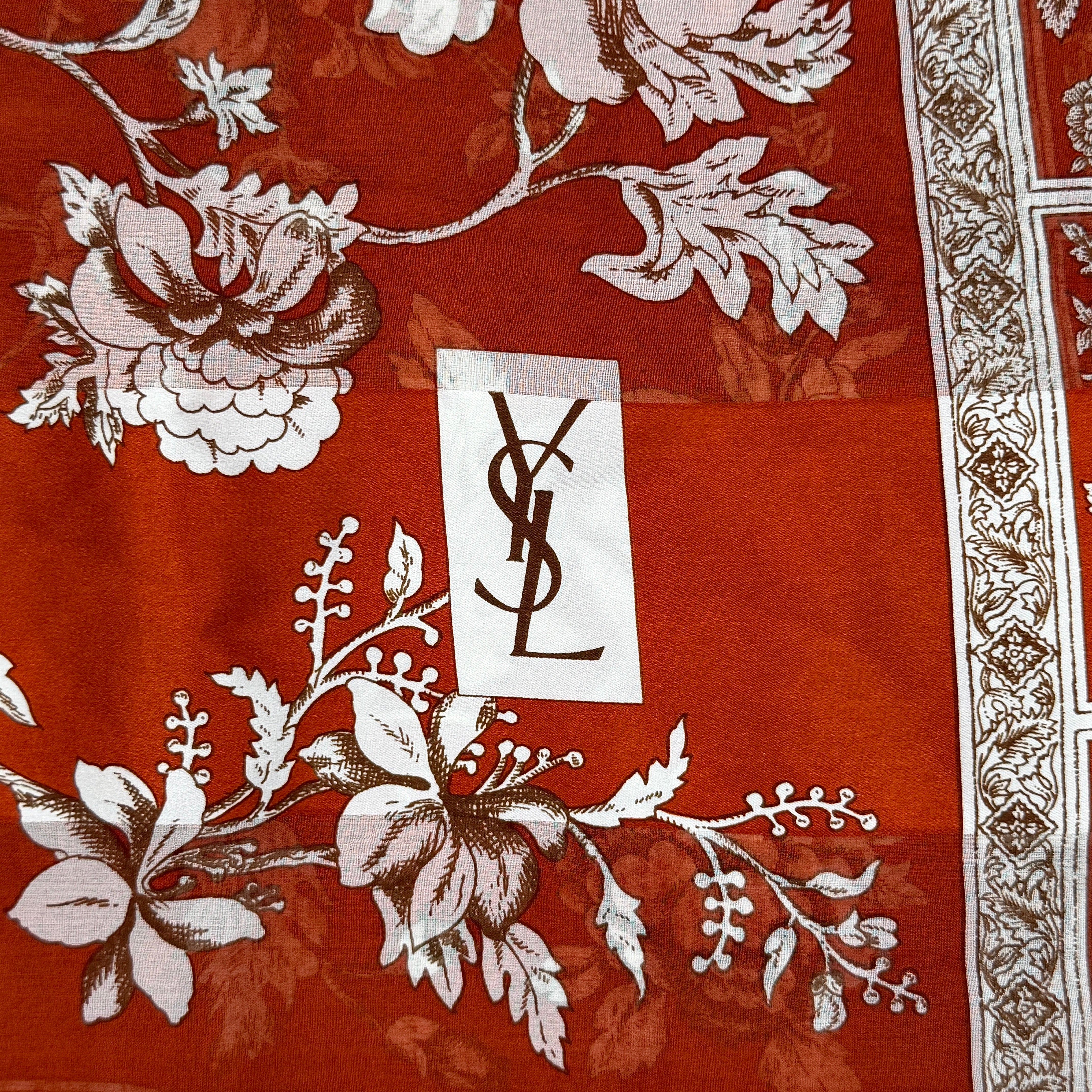 Saint Laurent silk scarf in rich red, featuring intricate cream floral designs and ornate borders with the YSL monogram visibly displayed.