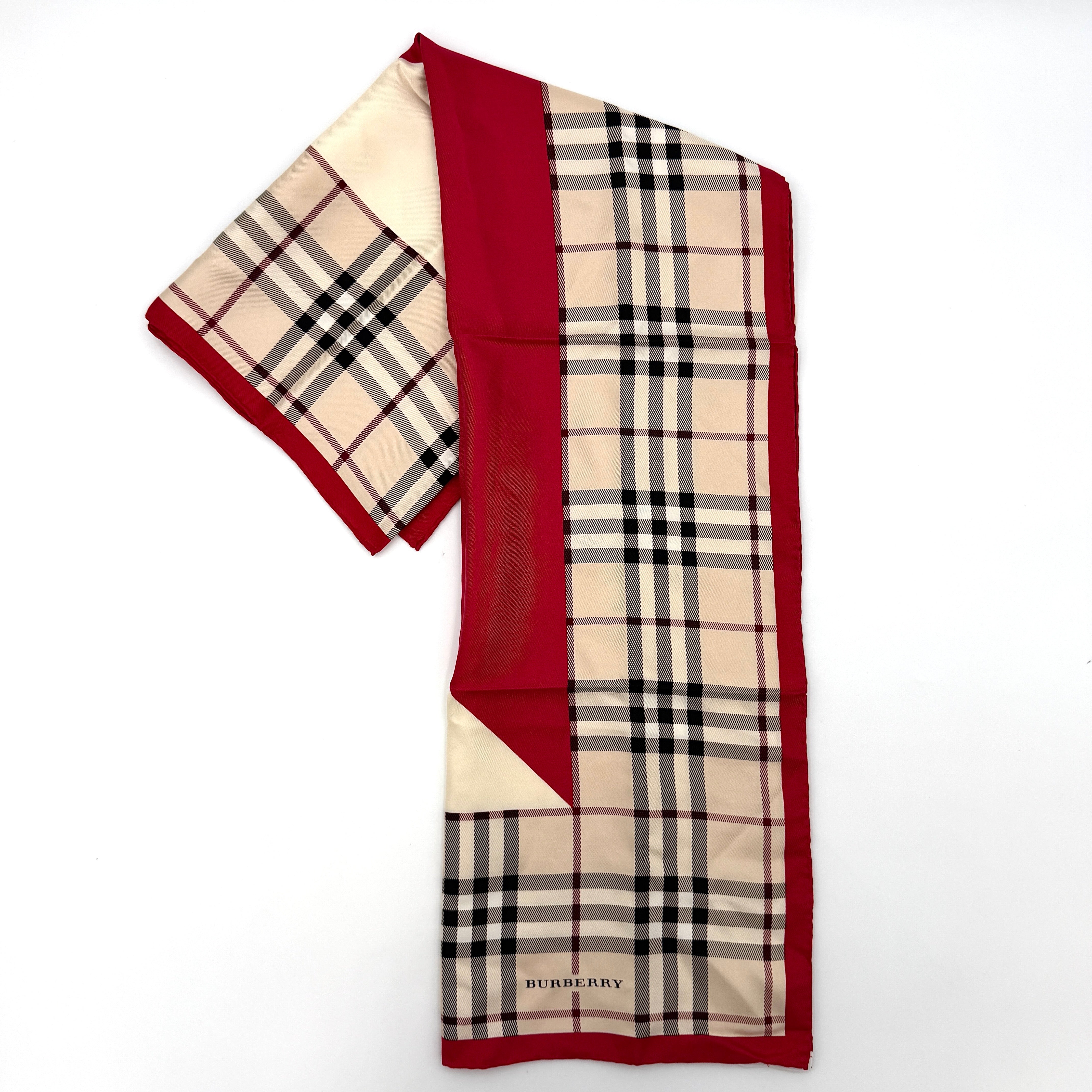 A Burberry silk scarf with beige check pattern, bold red borders, and ivory geometric panels, artfully arranged to showcase its contemporary elegance.