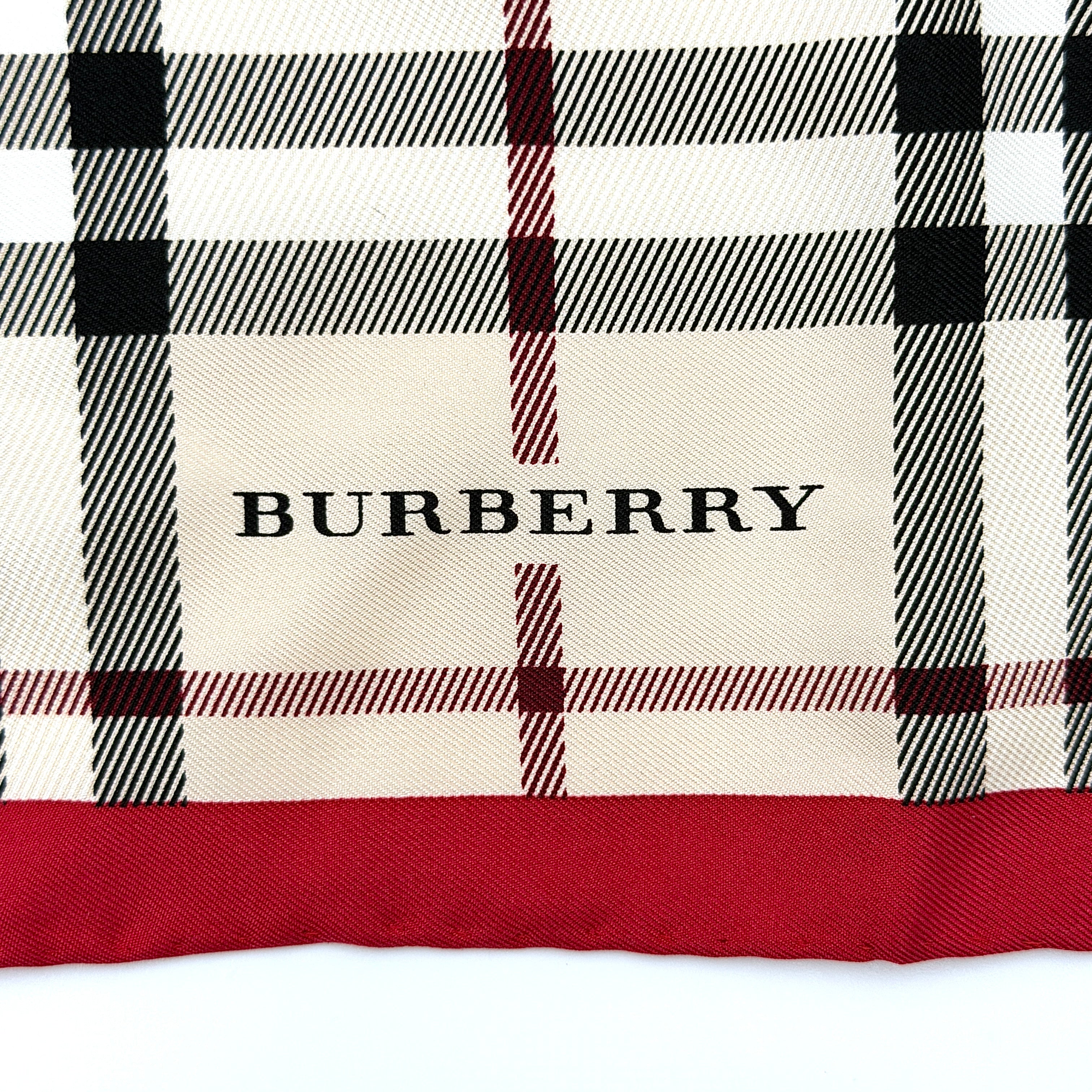 A Burberry silk scarf with beige check pattern, bold red borders, and ivory geometric panels, artfully arranged to showcase its contemporary elegance.