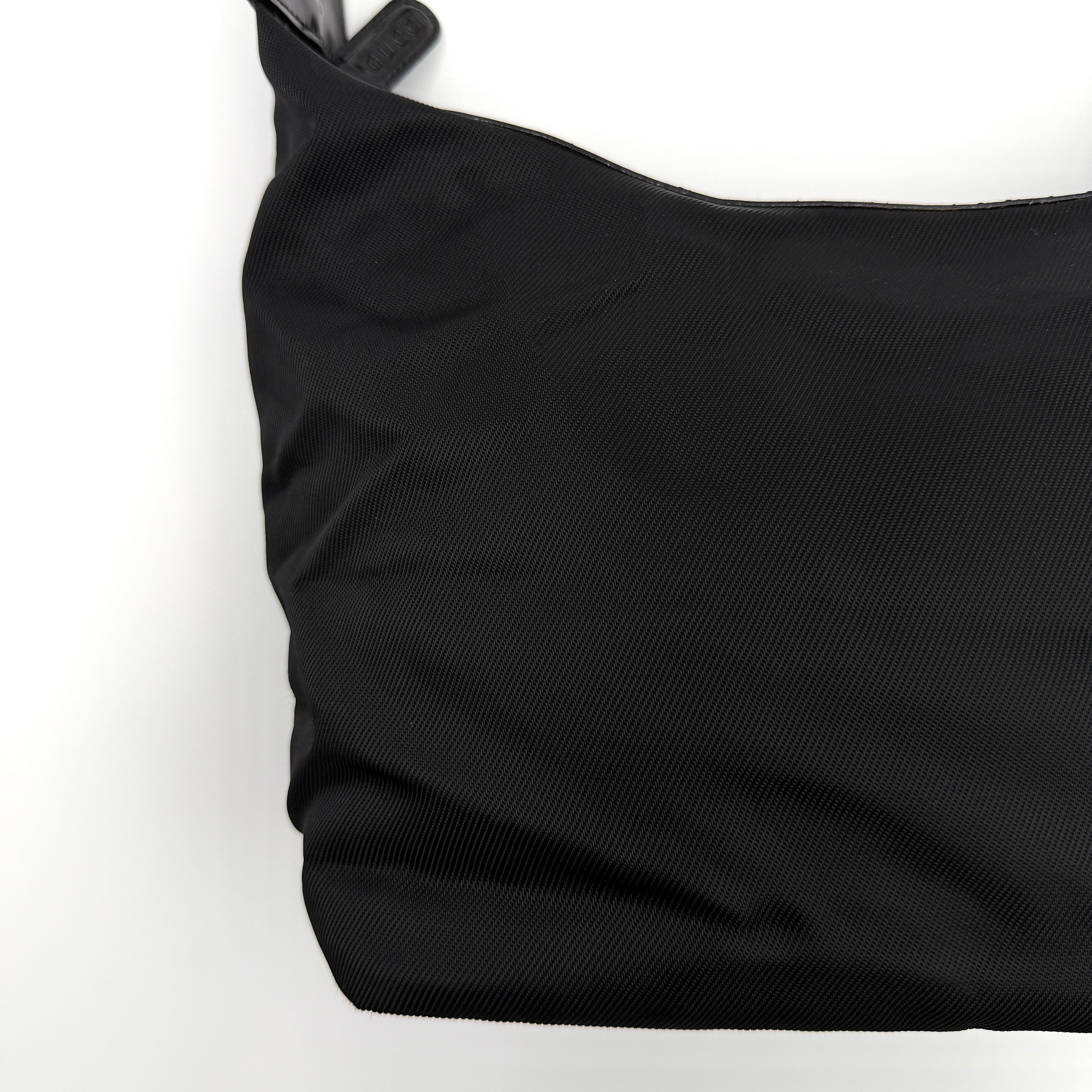 Gucci black nylon shoulder bag with a sculpted bamboo top handle and sleek silhouette against a white background.