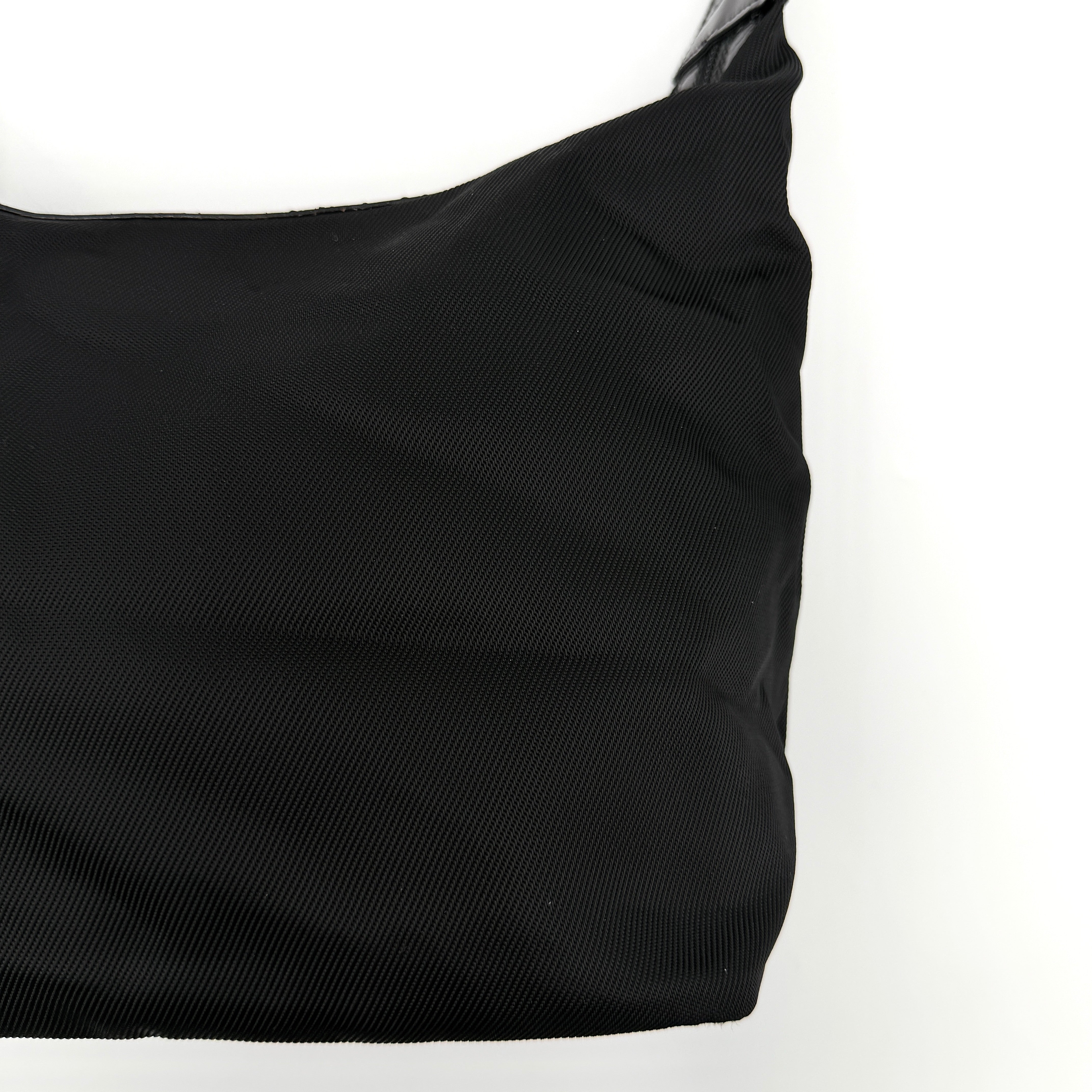 Gucci black nylon shoulder bag with a sculpted bamboo top handle and sleek silhouette against a white background.