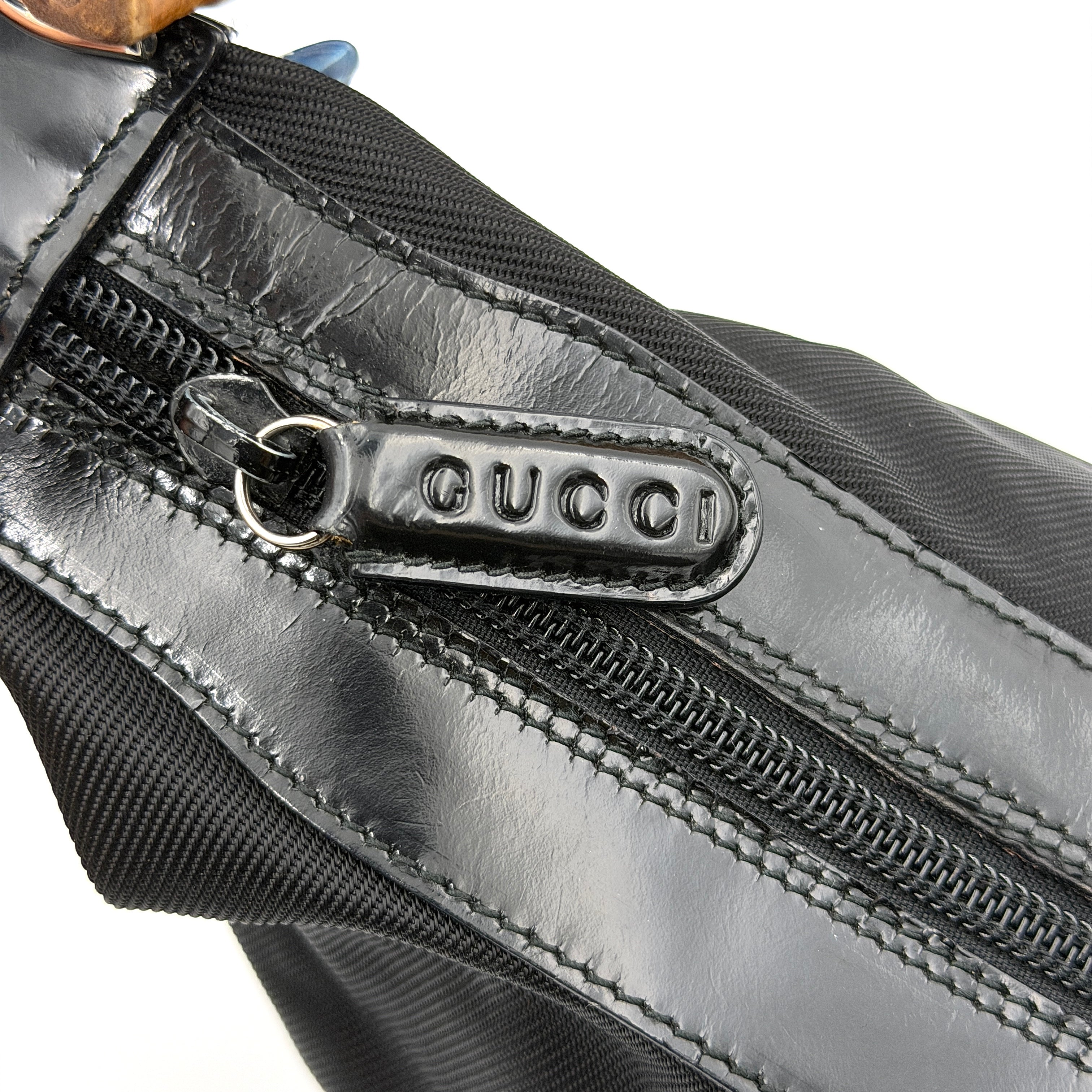 Gucci black nylon shoulder bag with a sculpted bamboo top handle and sleek silhouette against a white background.