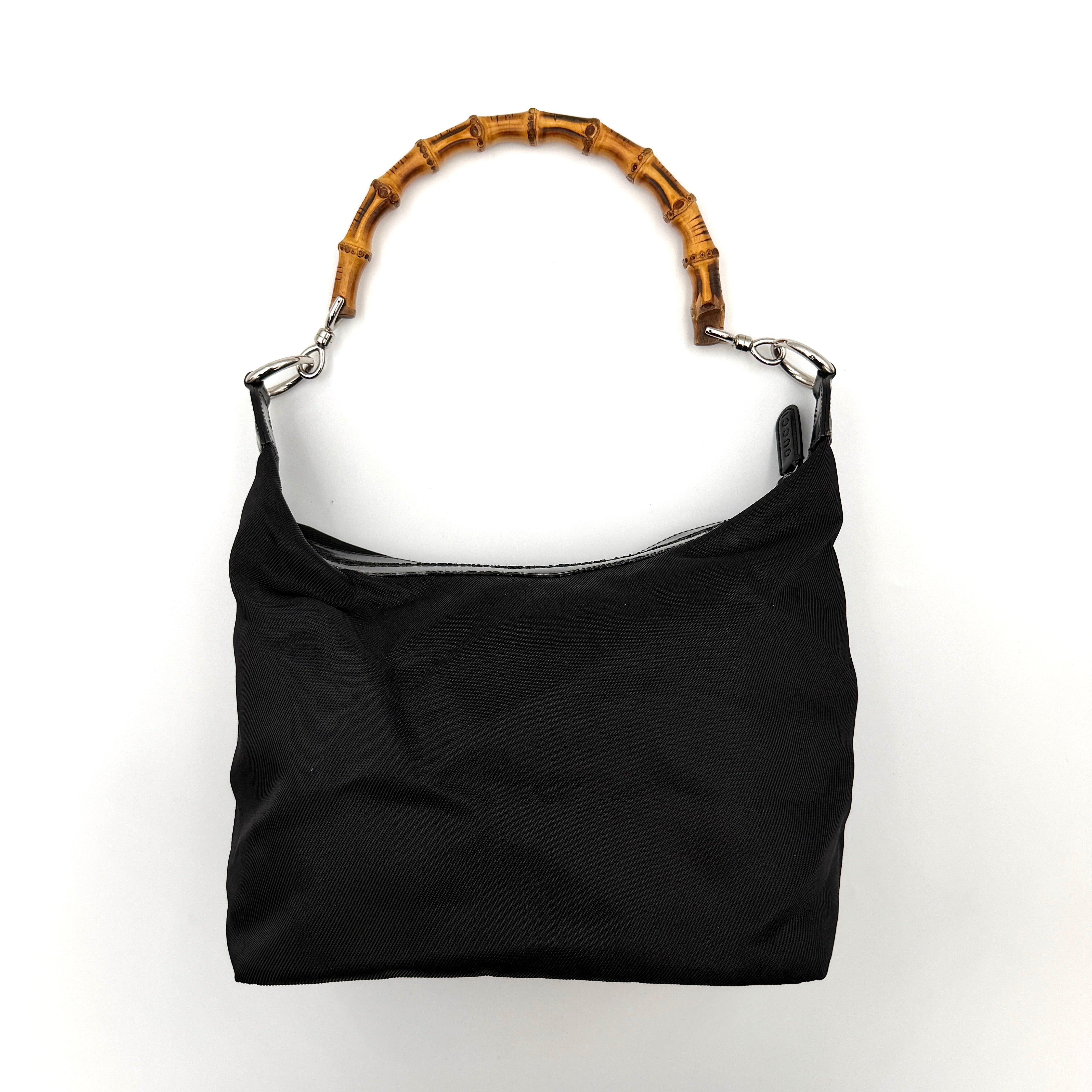 Gucci black nylon shoulder bag with a sculpted bamboo top handle and sleek silhouette against a white background.