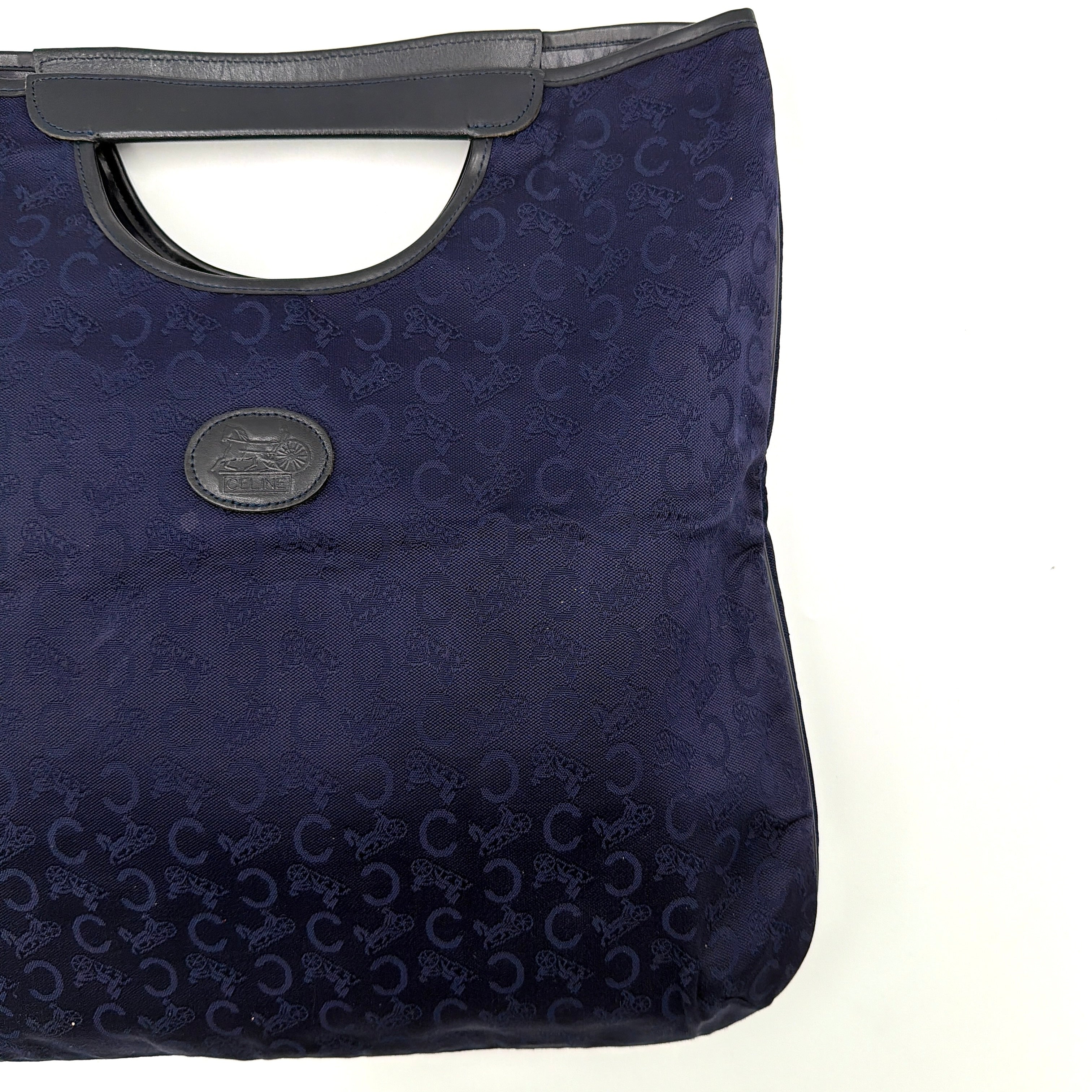 Celine Noevir Macadam Foldover Tote in navy jacquard with carriage motif, leather trim and cutout handles, photographed against a white background.