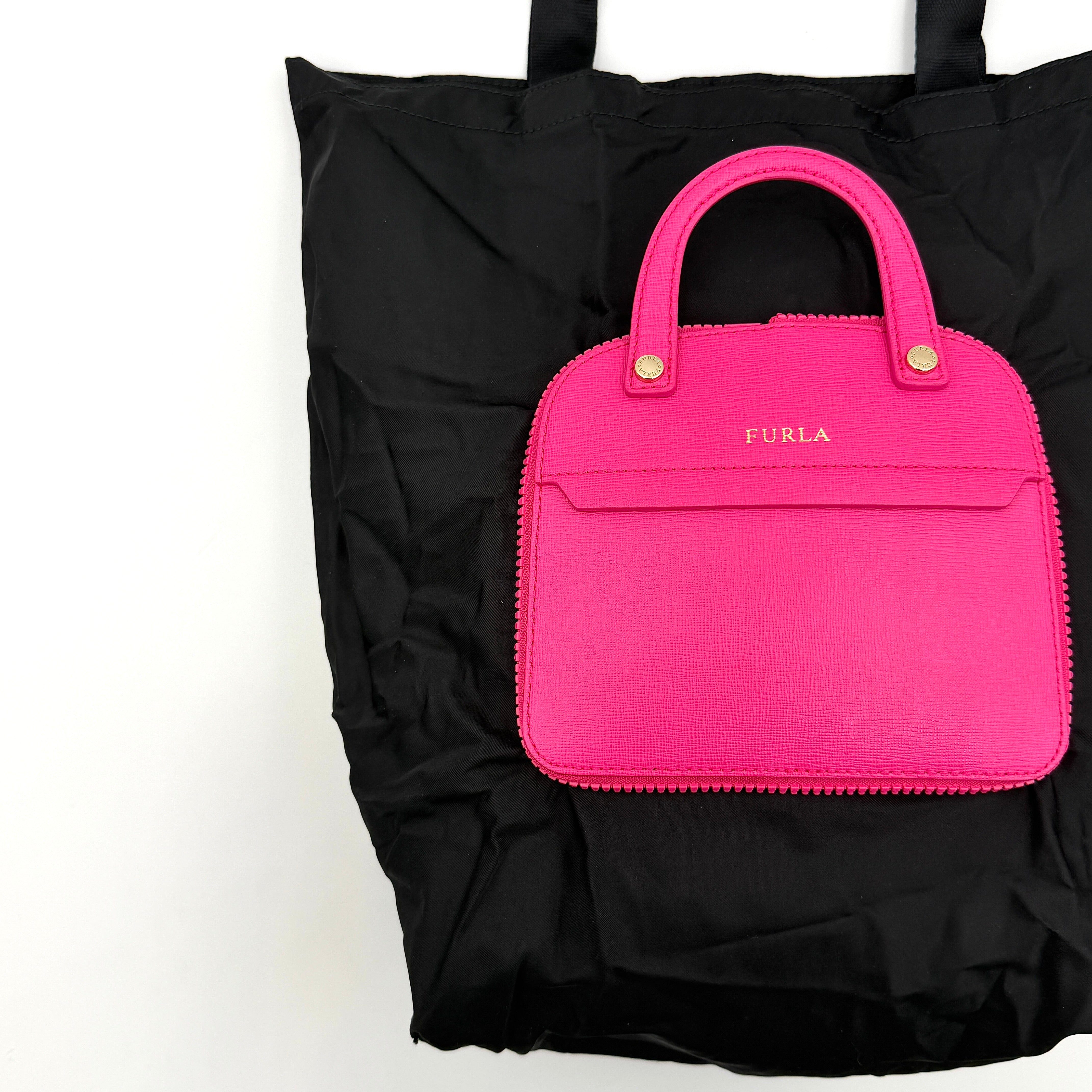 Furla black nylon tote bag with a bold pink zip pouch detail, styled as an exterior pocket, displayed flat to showcase its silhouette.