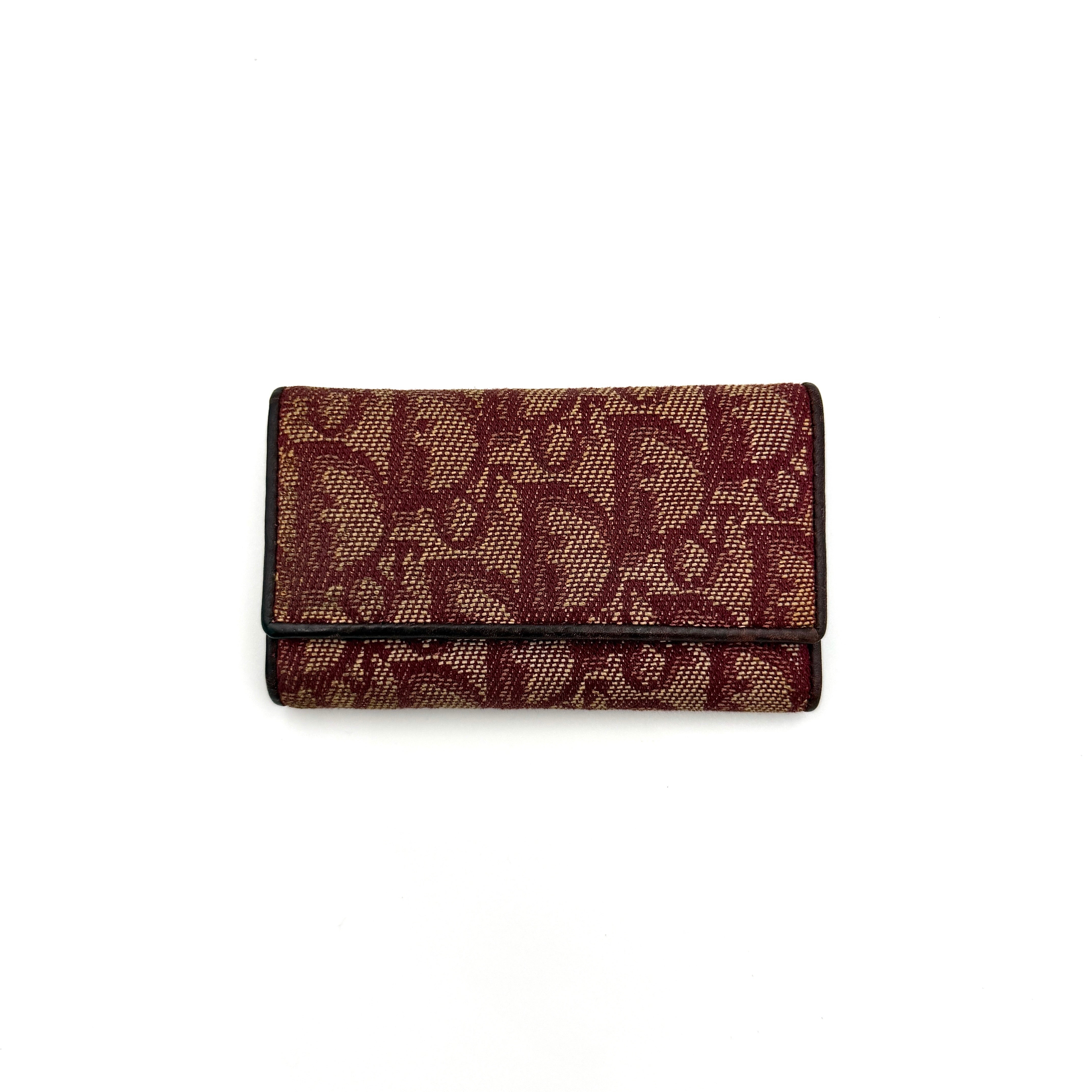 Dior Trotter Monogram key holder in red canvas with burgundy leather trim, photographed closed on a clean white background.