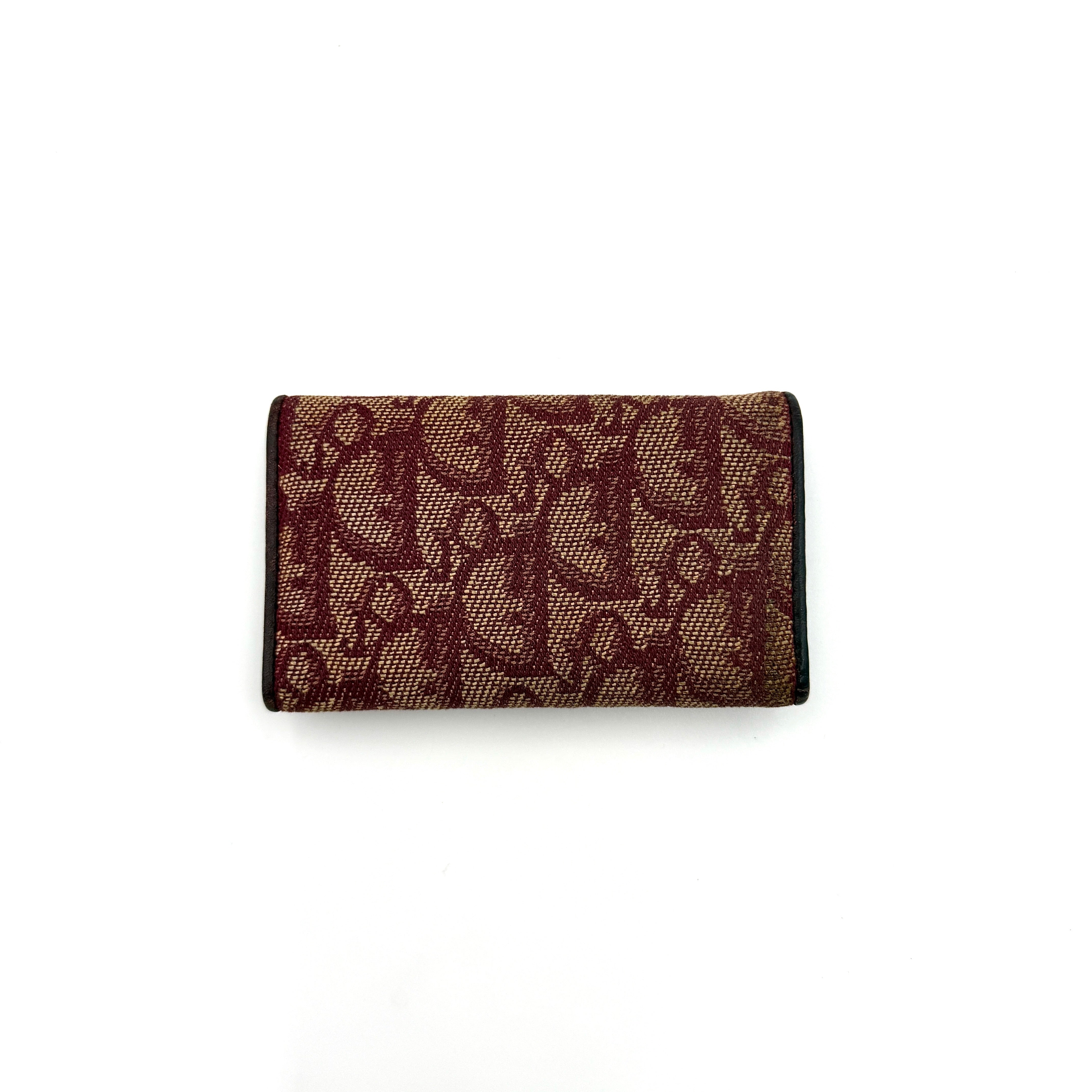 Dior Trotter Monogram key holder in red canvas with burgundy leather trim, photographed closed on a clean white background.
