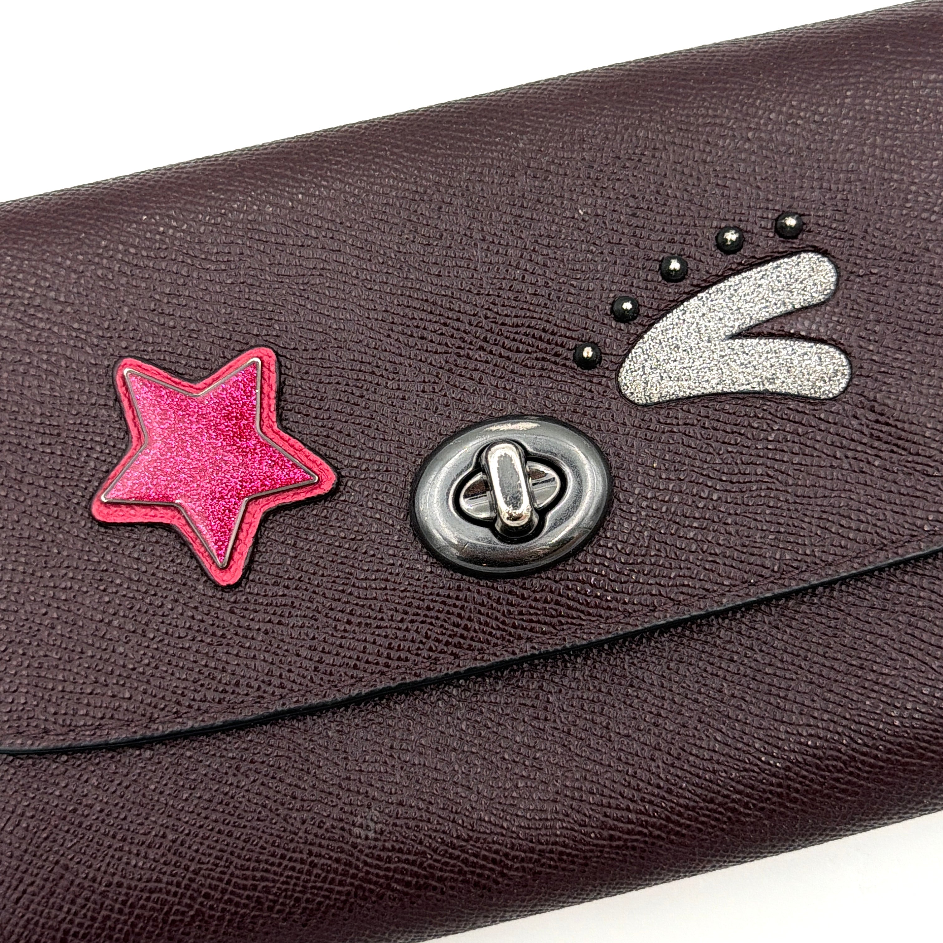 Coach Bear Turnlock Clutch in burgundy leather with playful pink and silver star details and signature gunmetal turnlock front closure.