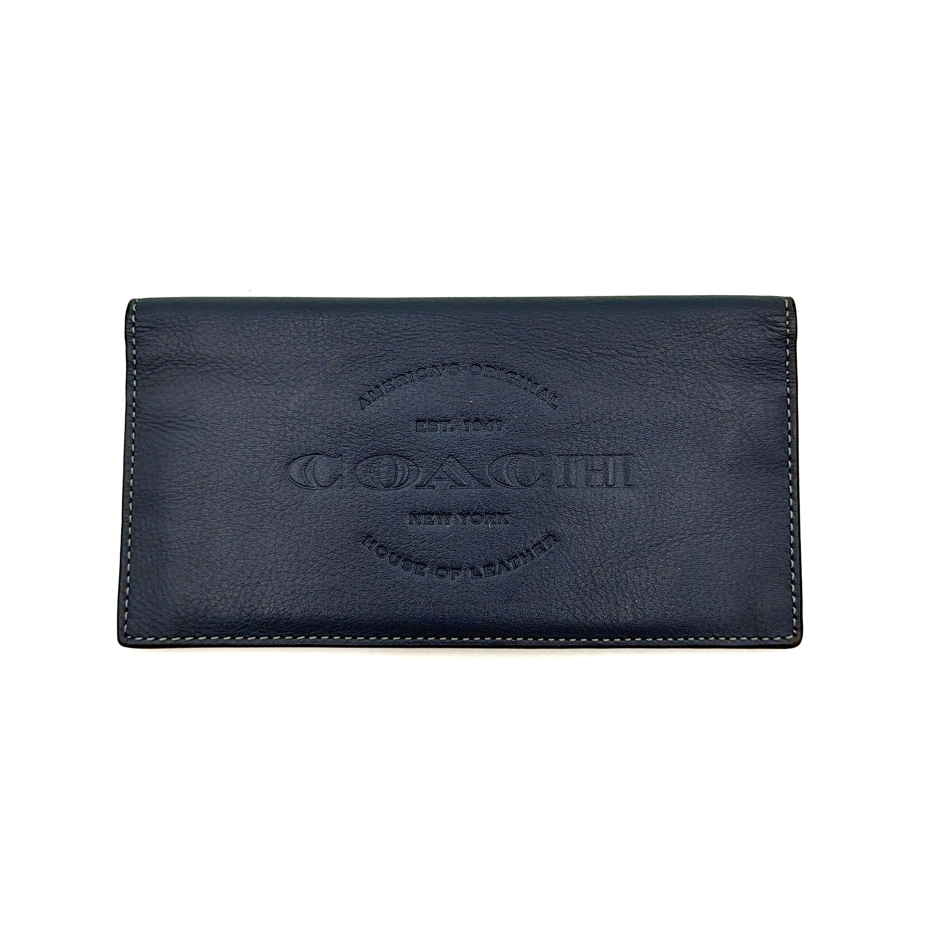 Coach Flap Long Wallet in navy blue leather with embossed logo, shown in a crisp editorial front view.