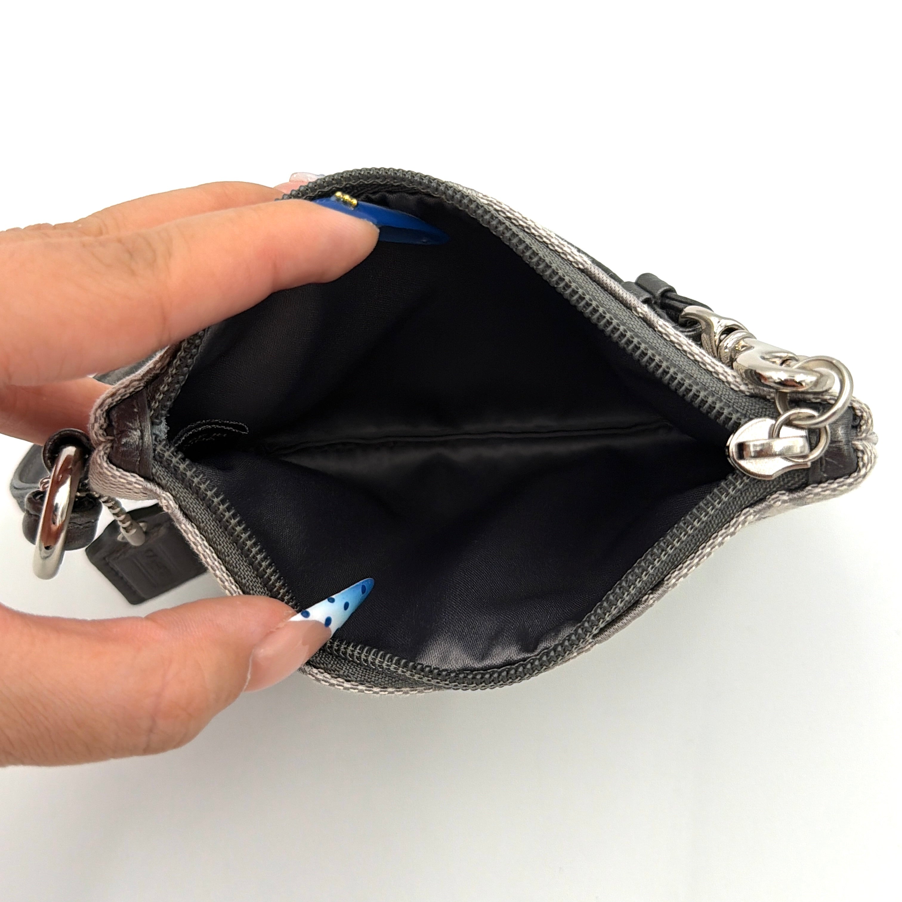 Coach Signature Canvas Corner Zip Wristlet in grey with monogram print, silver oval logo plaque, and black leather wrist strap.