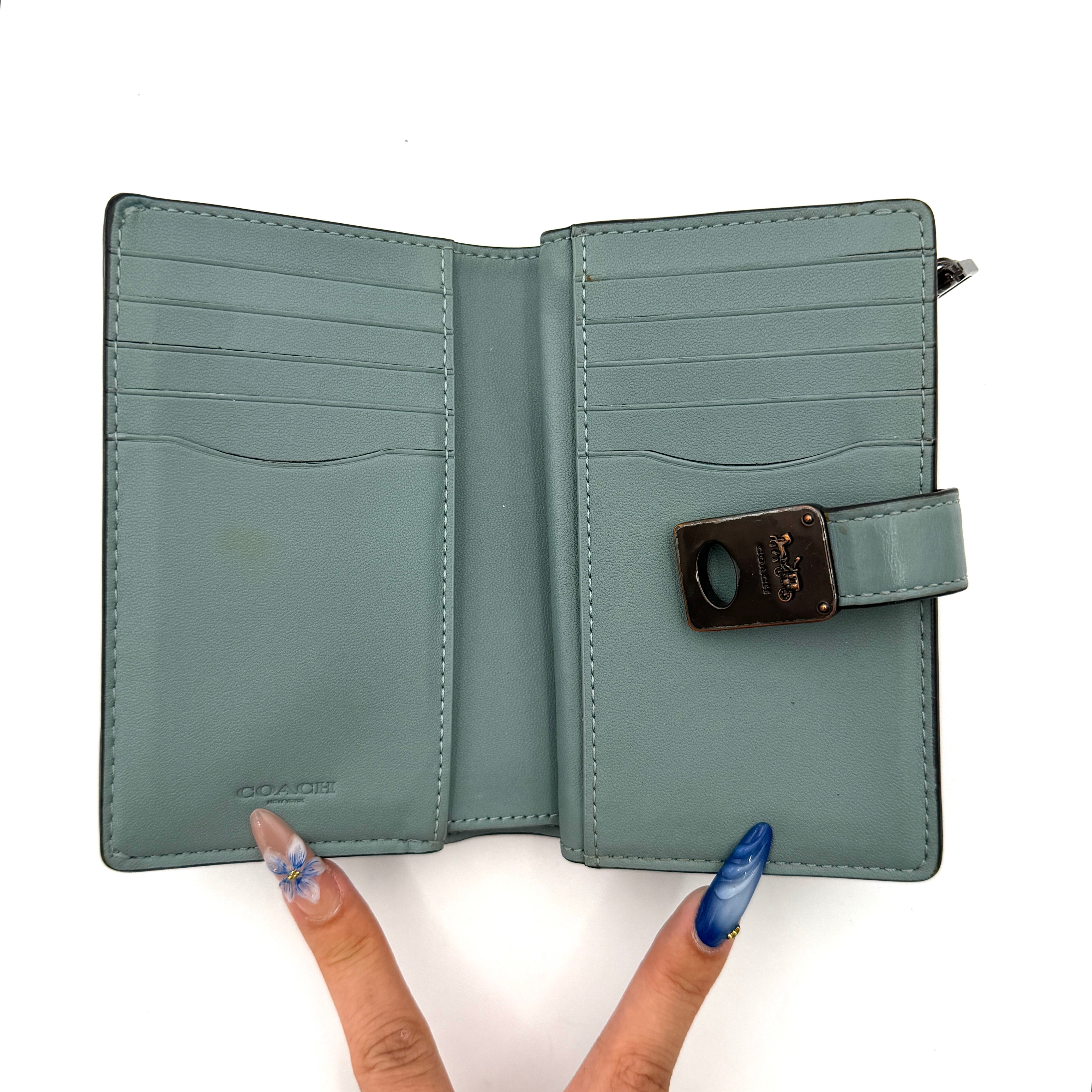 Coach Hutton Turnlock Wallet in light blue leather with signature gold turnlock clasp, showcased from the front.