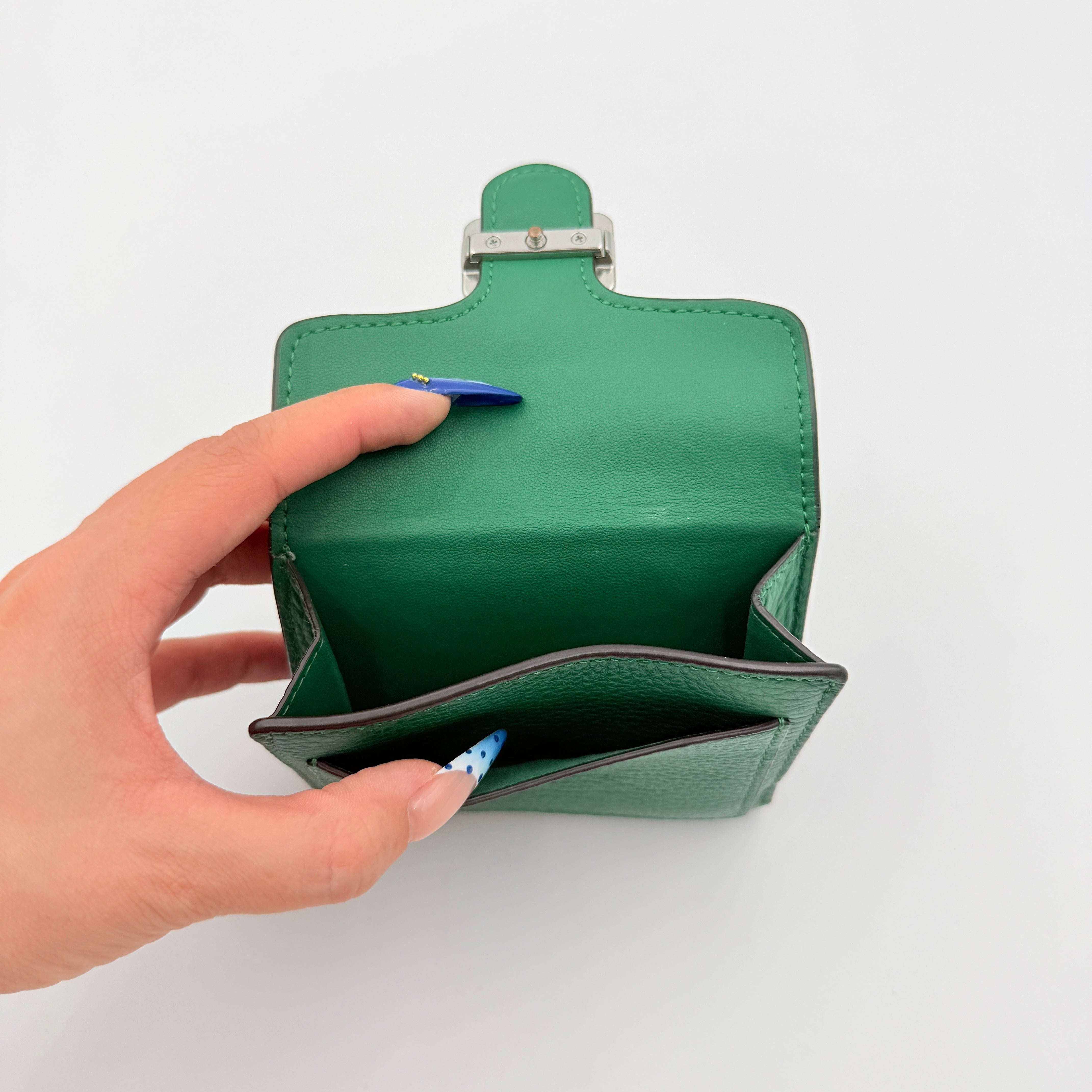 Coach Pepper Leather Wallet in emerald green pebbled leather with a front flap and enamel logo plaque, displayed neatly against a white background.