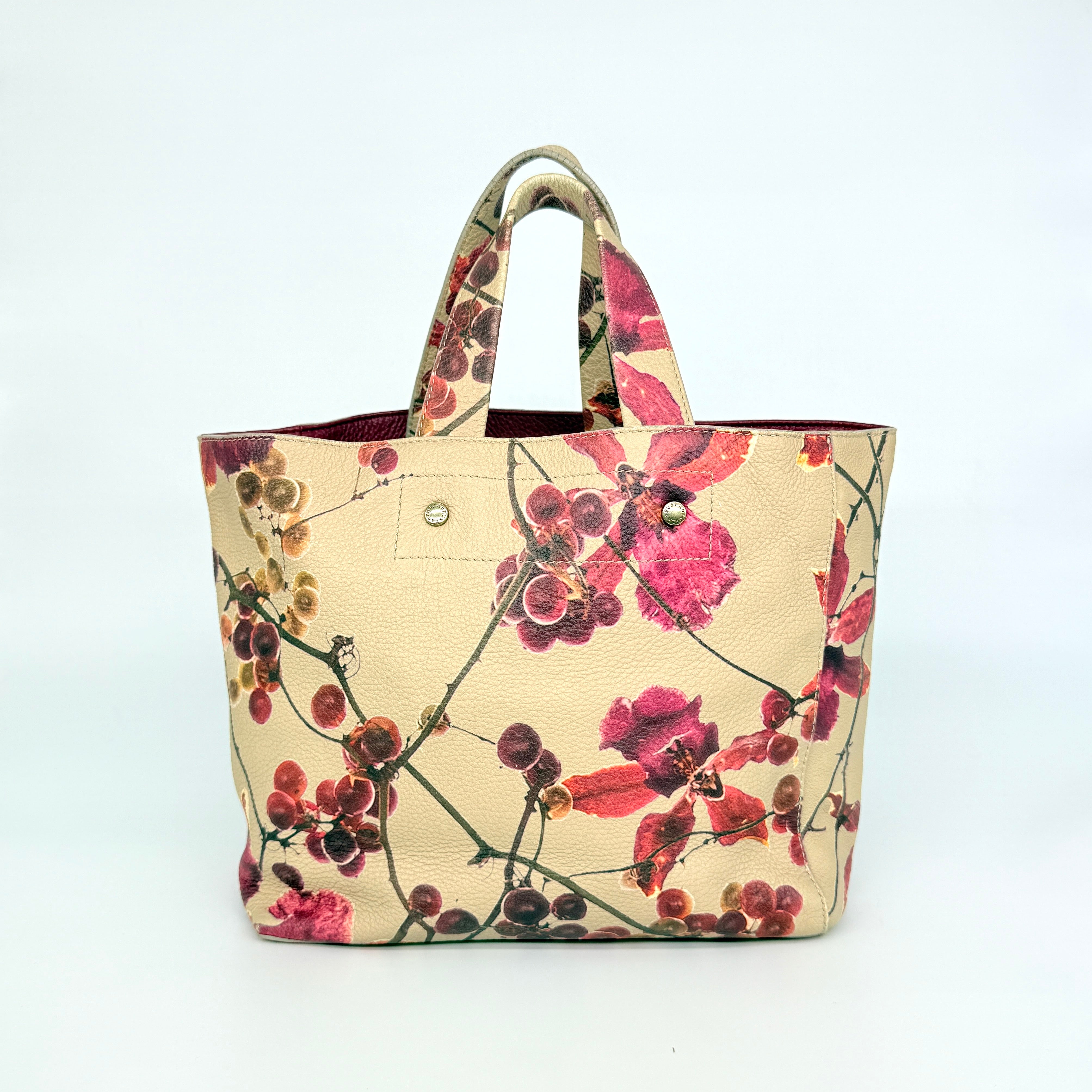 Furla beige leather tote bag adorned with a bold magenta and plum floral print, featuring structured short handles.
