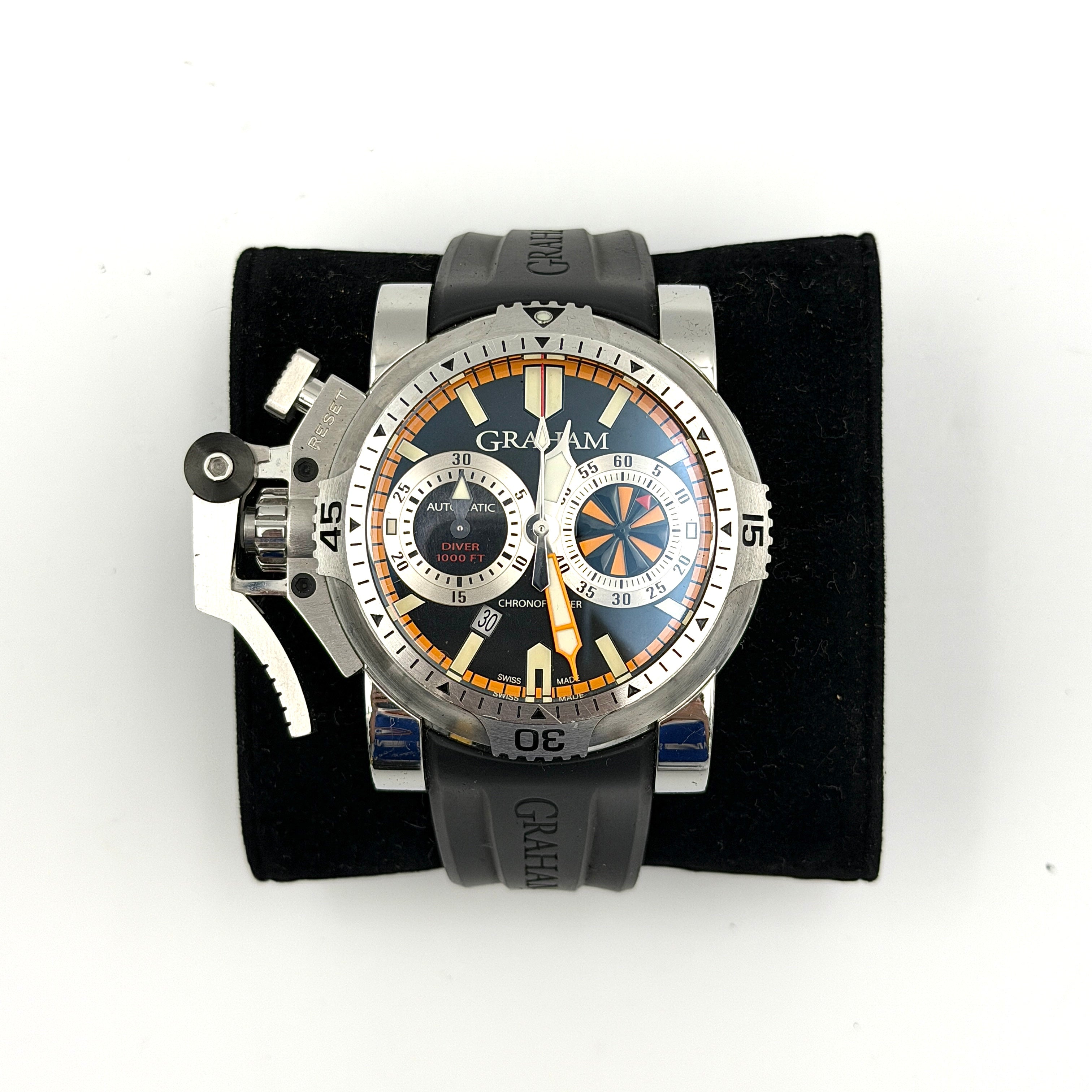 The Graham Chronofighter Oversize Diver 2OVES.B15A watch displayed in its signature round Graham London presentation case, showcasing its bold black dial, prominent chronograph trigger, and black rubber strap.