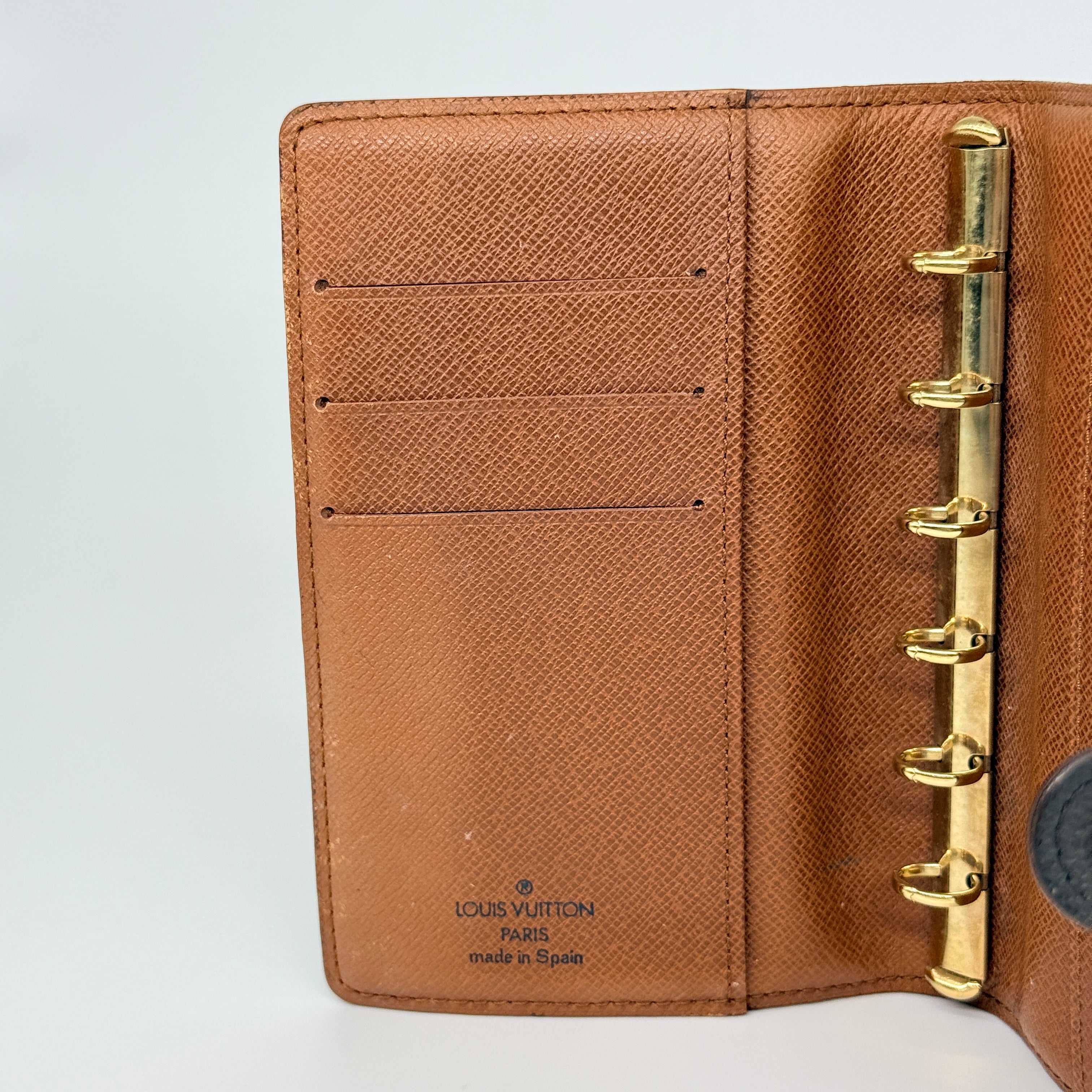 Louis Vuitton Monogram Agenda Cover in brown canvas with gold snap closure, displayed against a white background.