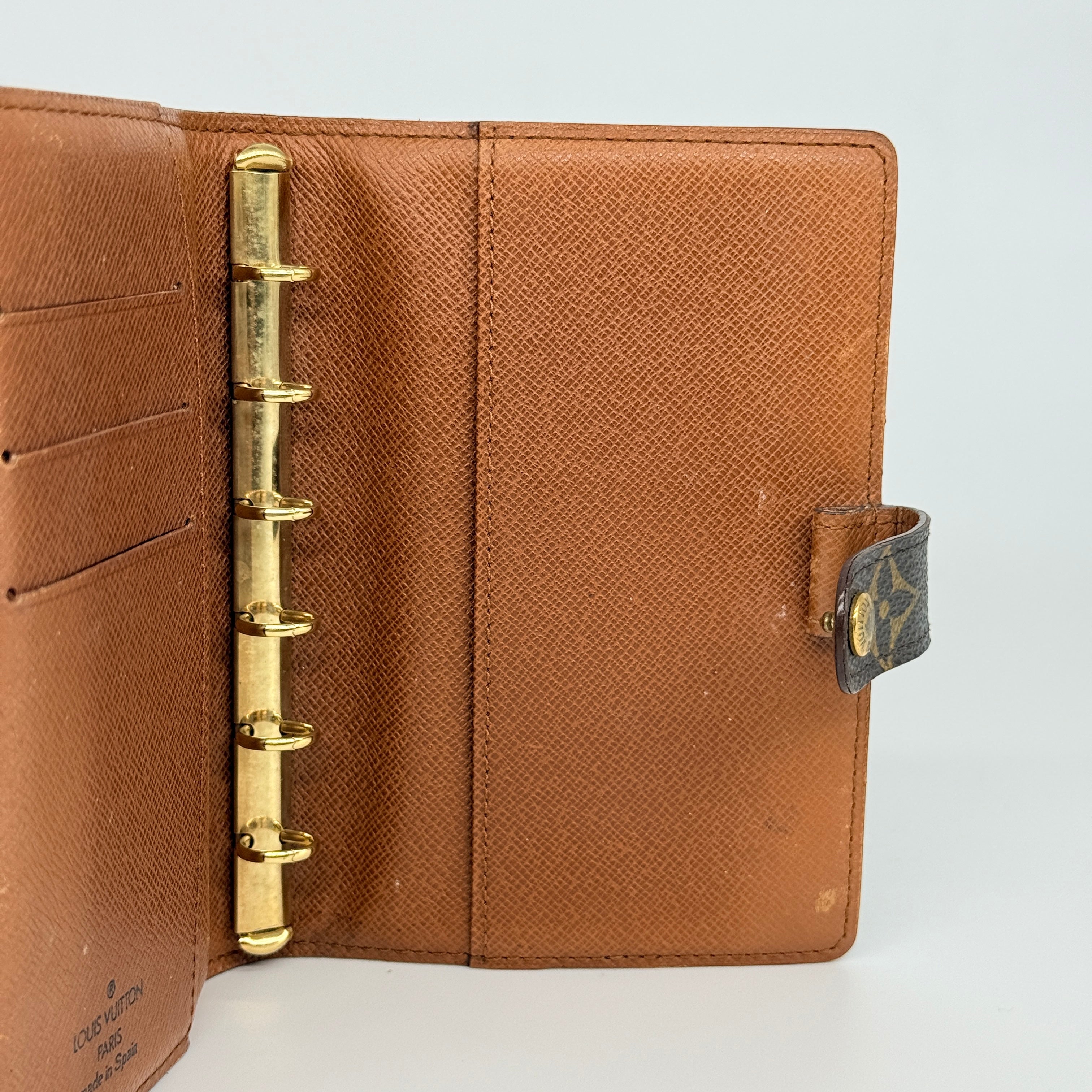 Louis Vuitton Monogram Agenda Cover in brown canvas with gold snap closure, displayed against a white background.