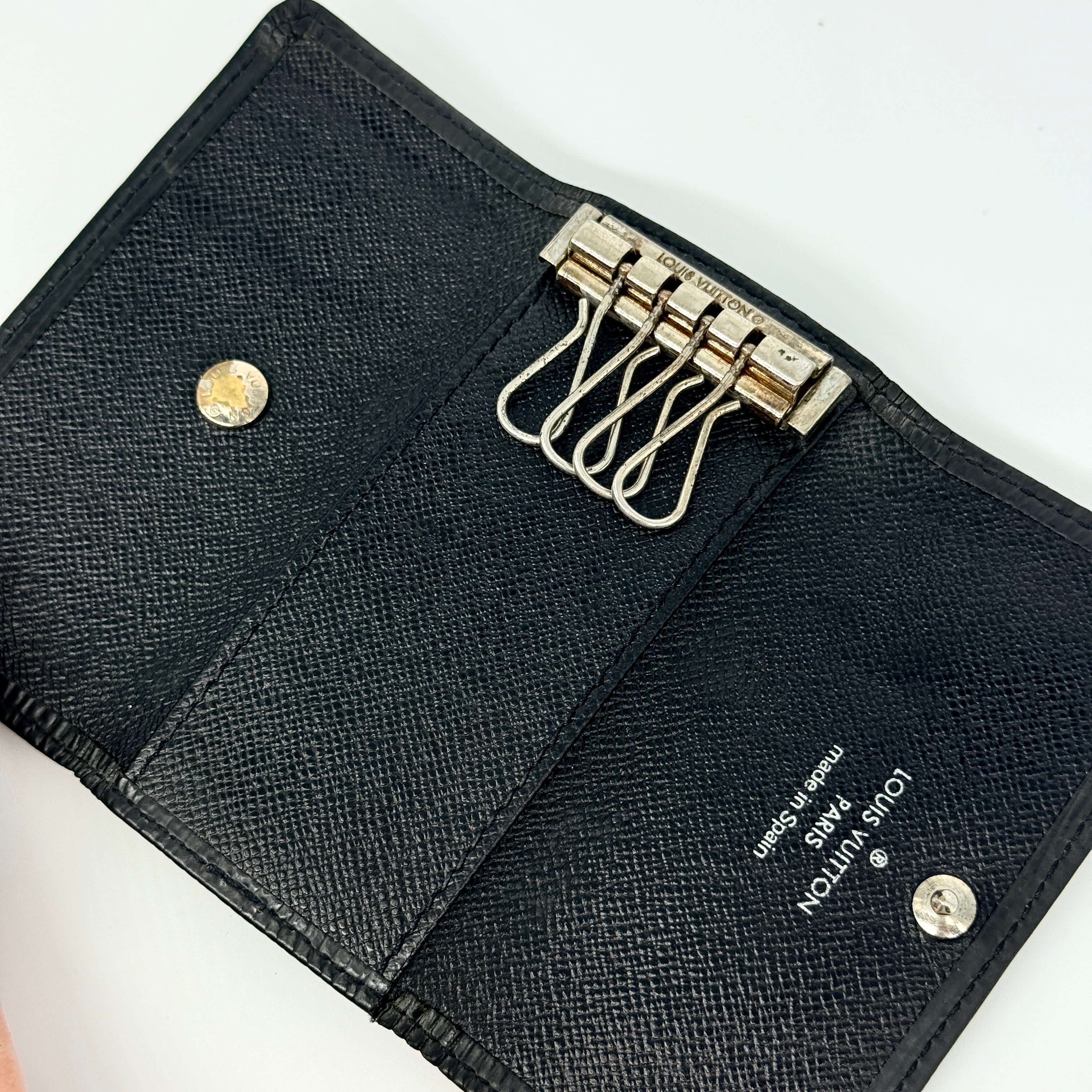 Louis Vuitton Epi Leather key case in black with silver-tone key hooks and snap closure, photographed against a clean white background.