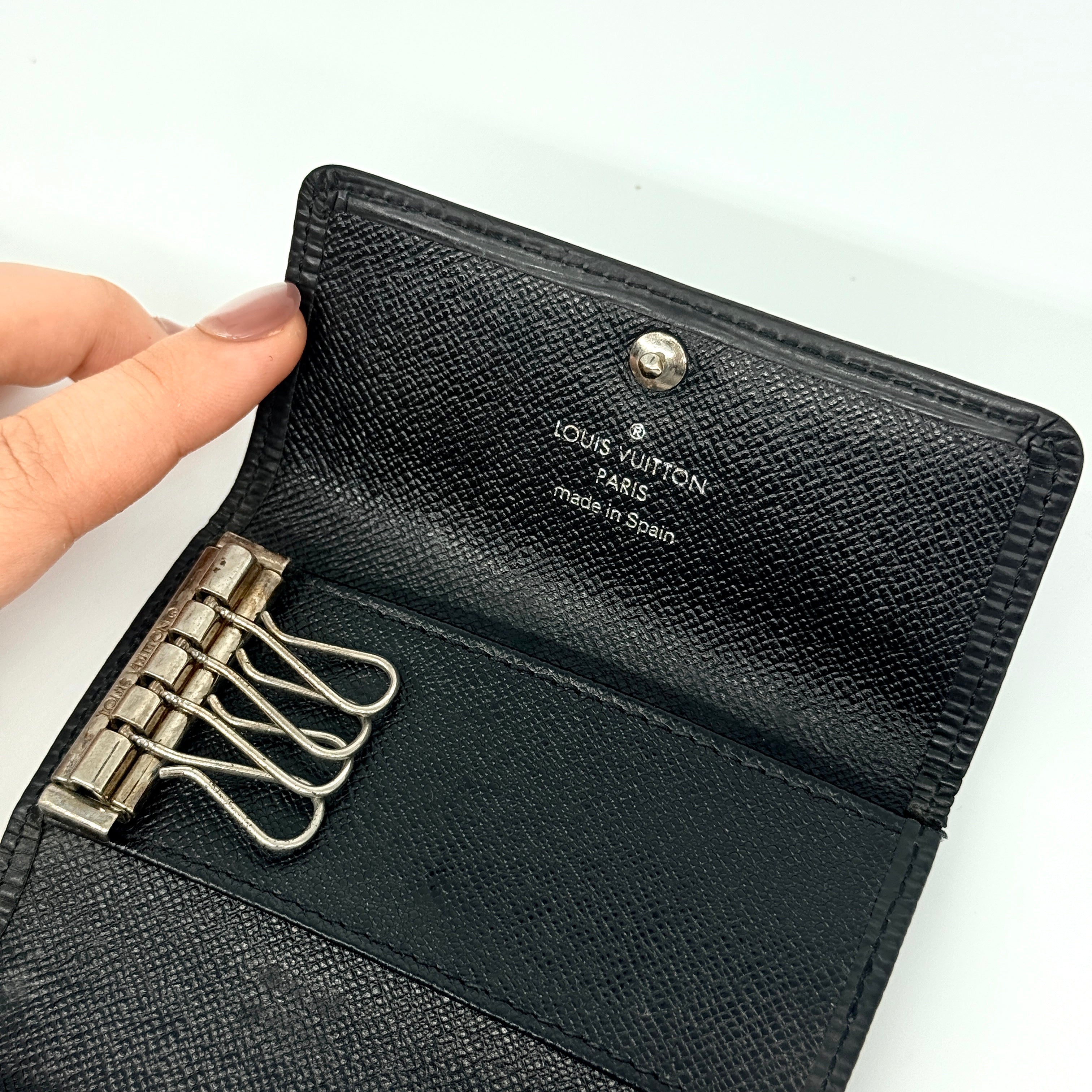 Louis Vuitton Epi Leather key case in black with silver-tone key hooks and snap closure, photographed against a clean white background.