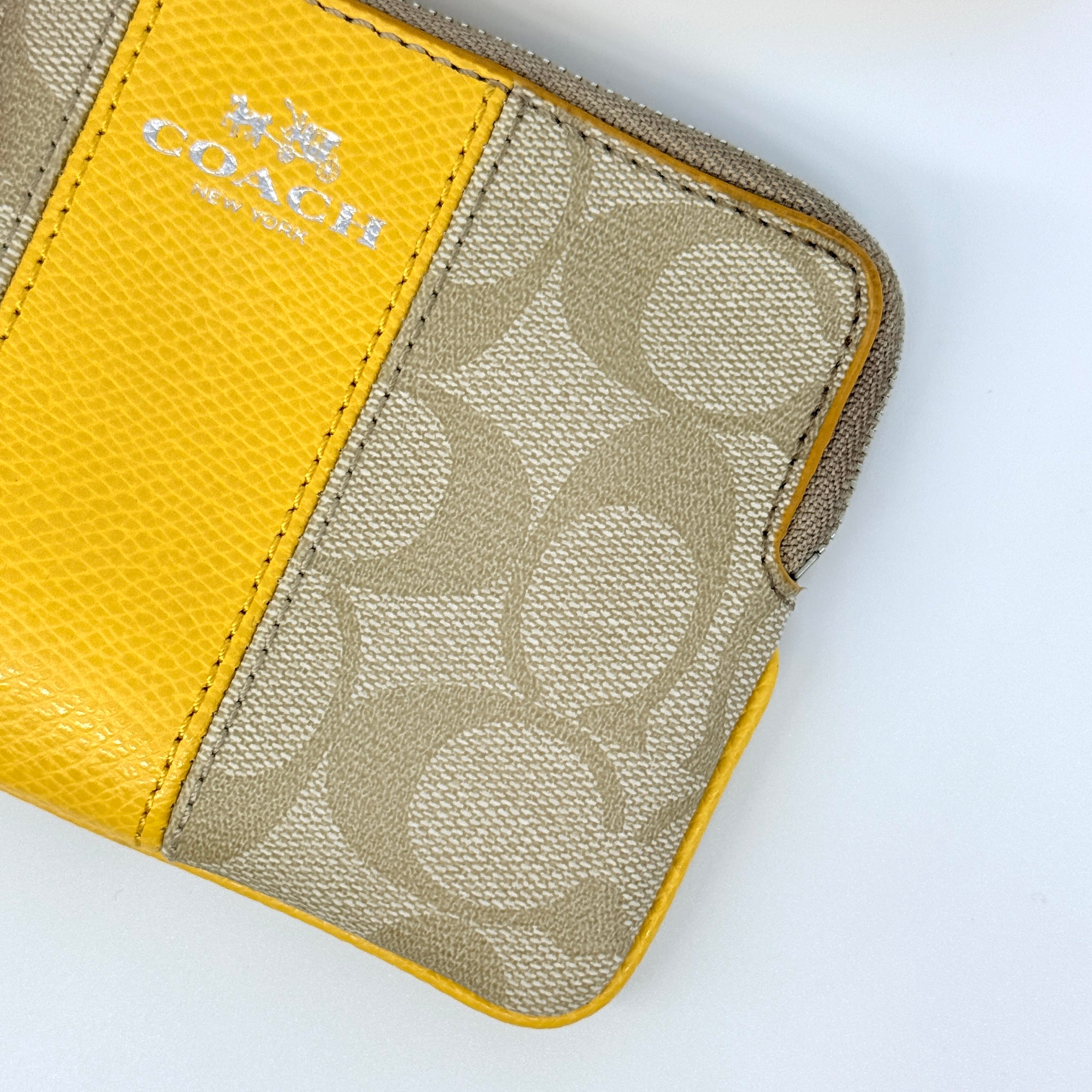 Coach Signature Stripe Corner Zip Wristlet in beige canvas with bold yellow leather stripe, silver hardware, and wrist strap displayed on a white background.