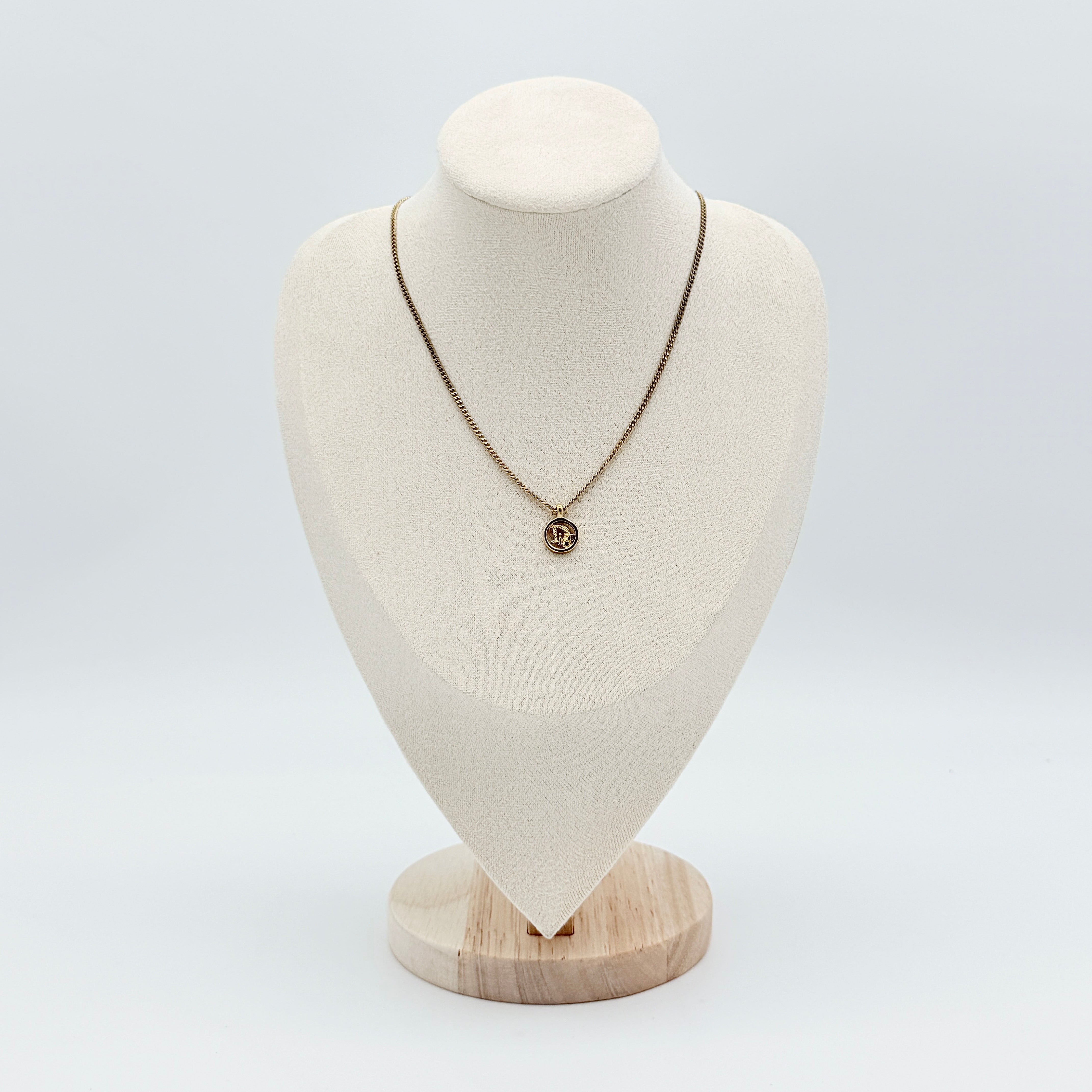 Dior gold-tone necklace featuring a circular logo pendant displayed on a necklace stand.