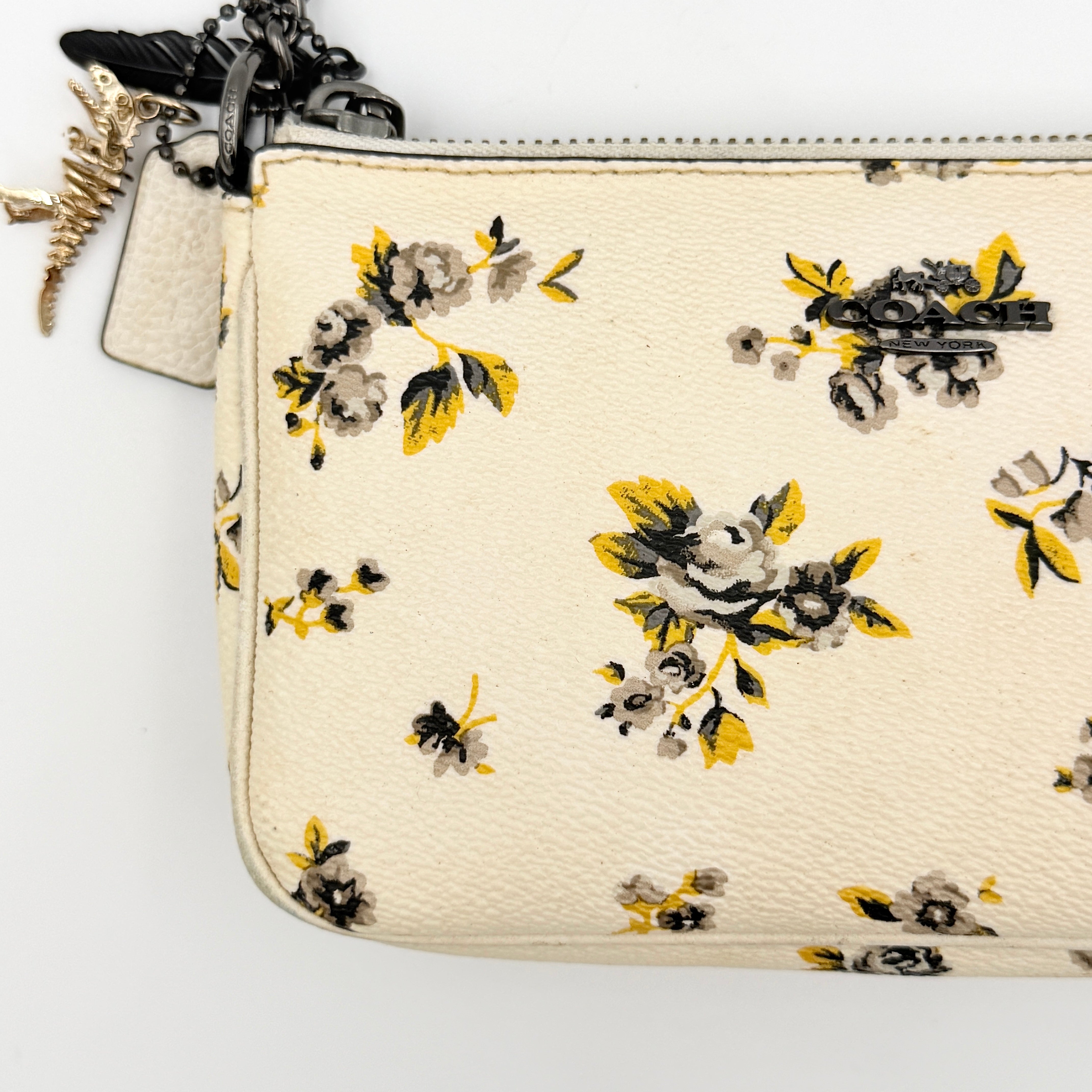 Coach Nolita 19 shoulder bag in white pebbled leather with yellow and grey floral print, chunky gunmetal chain strap, and decorative charms.