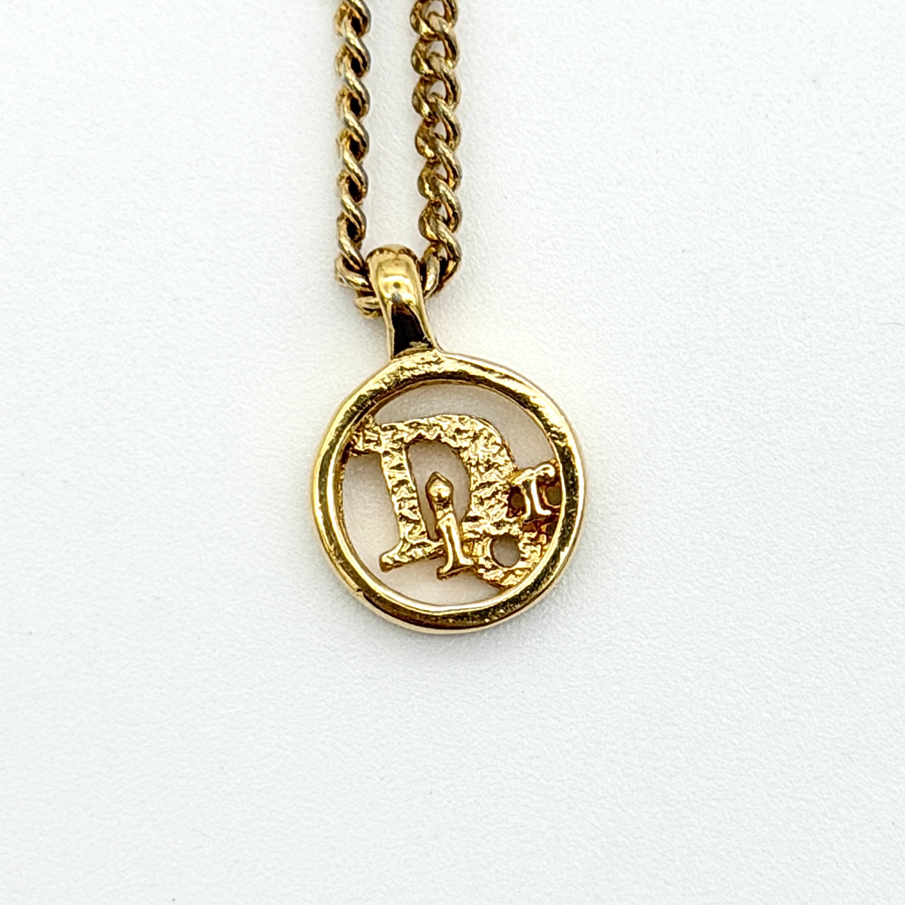Dior gold-tone necklace featuring a circular logo pendant displayed on a necklace stand.