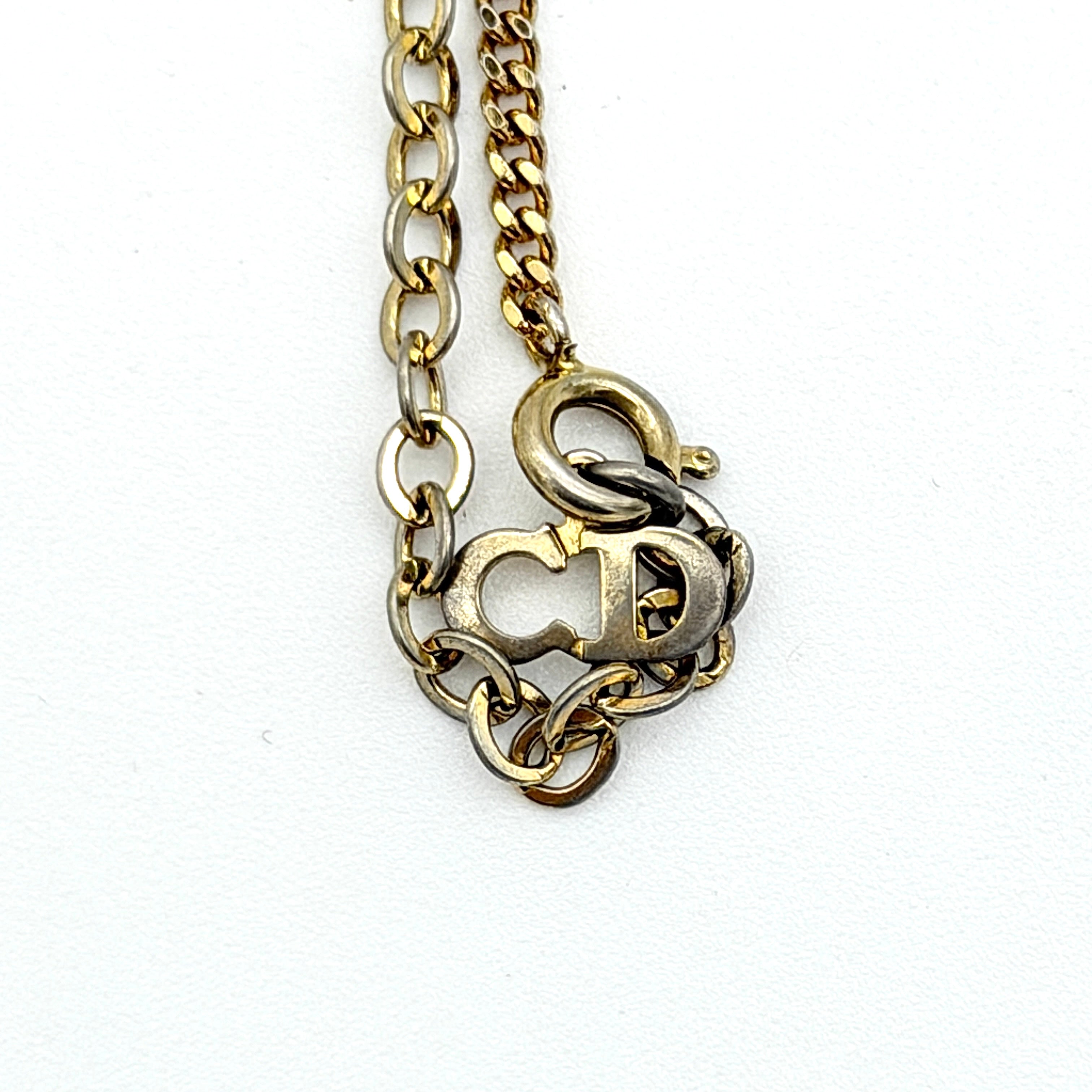 Dior gold-tone necklace featuring a circular logo pendant displayed on a necklace stand.