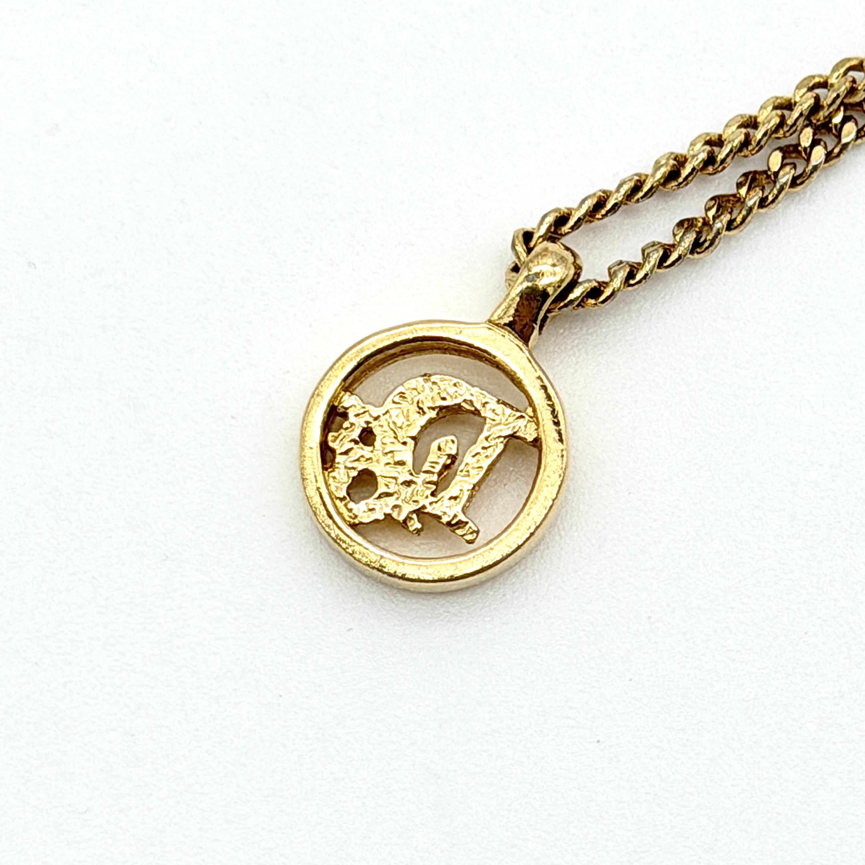Dior gold-tone necklace featuring a circular logo pendant displayed on a necklace stand.