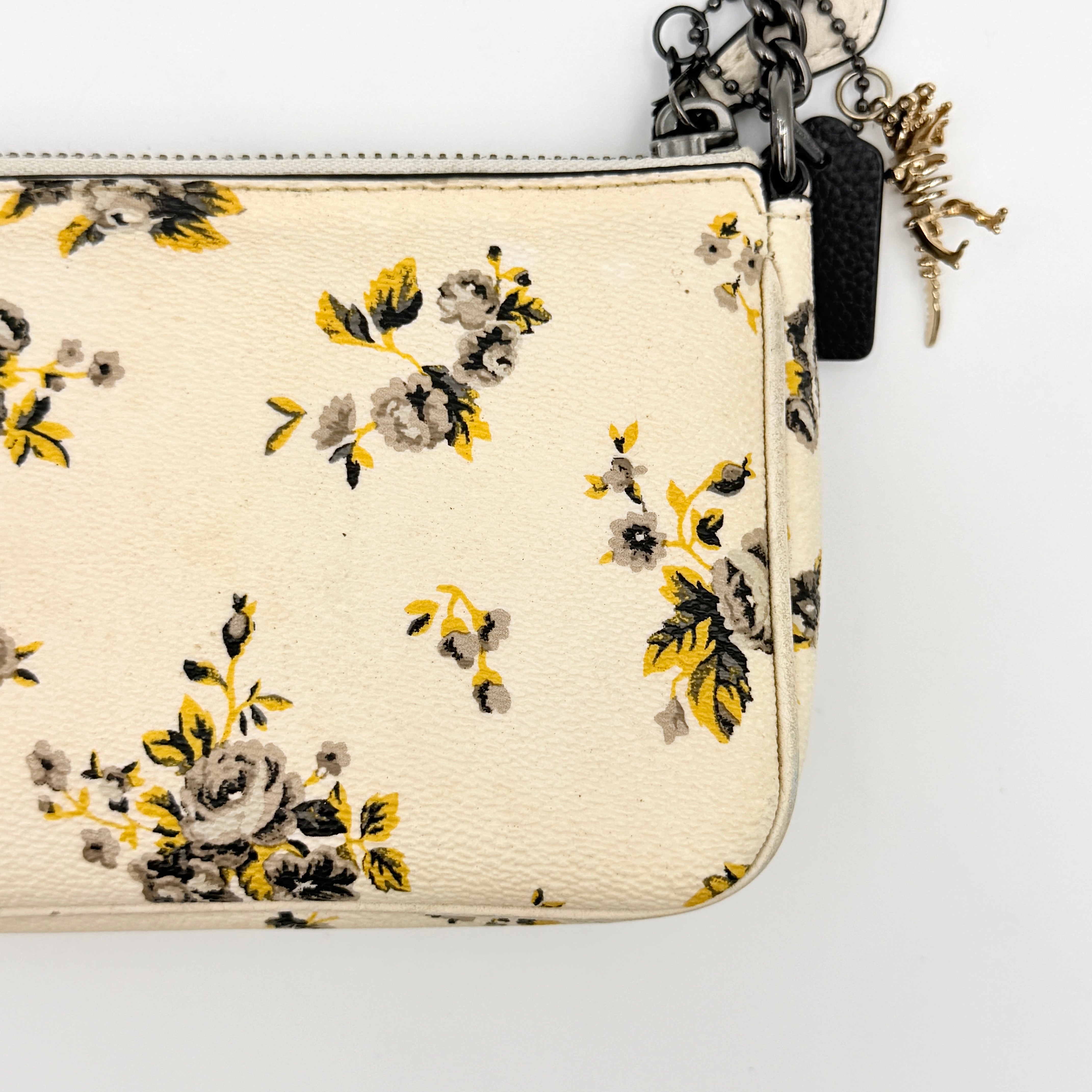 Coach Nolita 19 shoulder bag in white pebbled leather with yellow and grey floral print, chunky gunmetal chain strap, and decorative charms.
