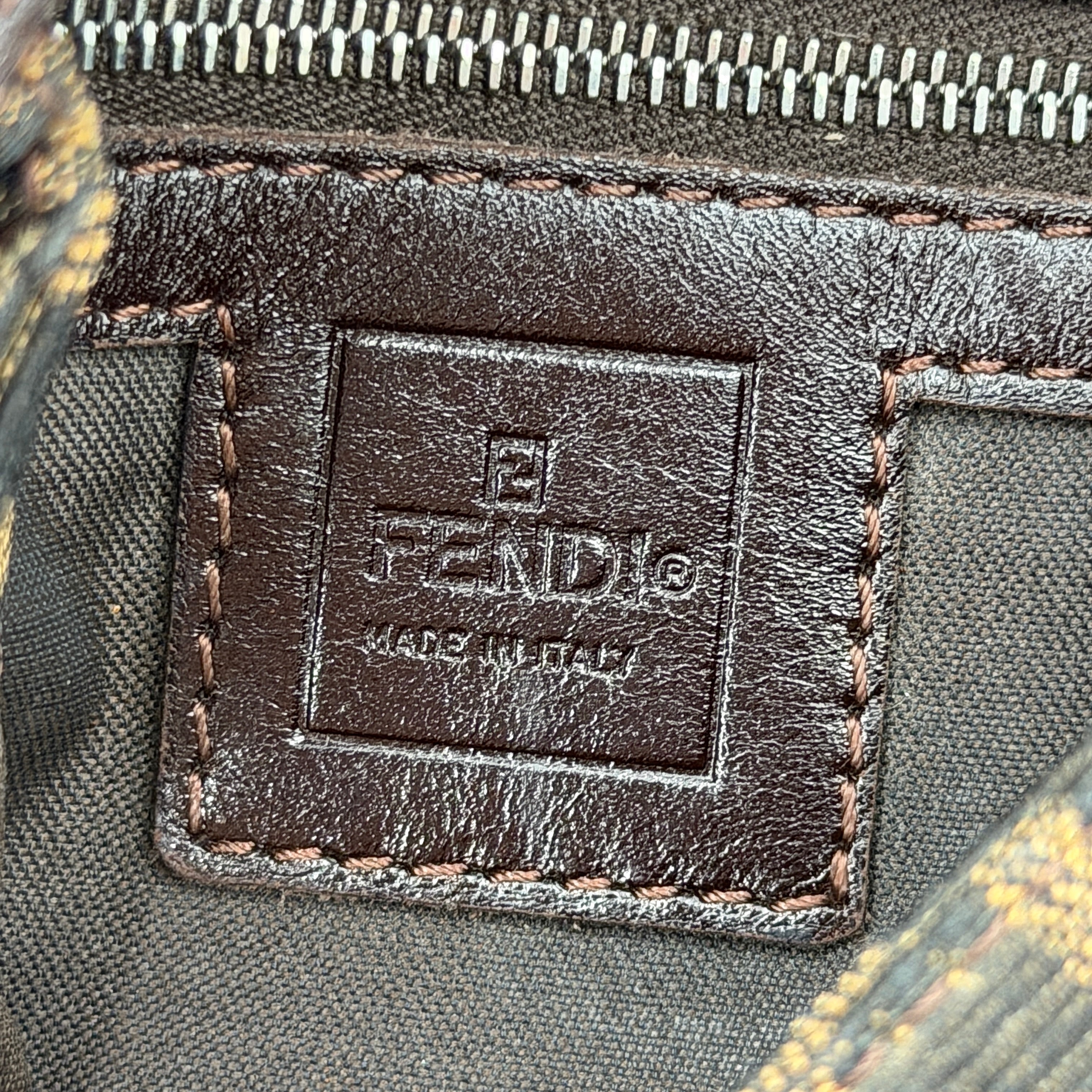 Fendi Zucca Print Baguette Bag in brown monogram canvas with silver-tone FF clasp and leather trim shown against a white background.