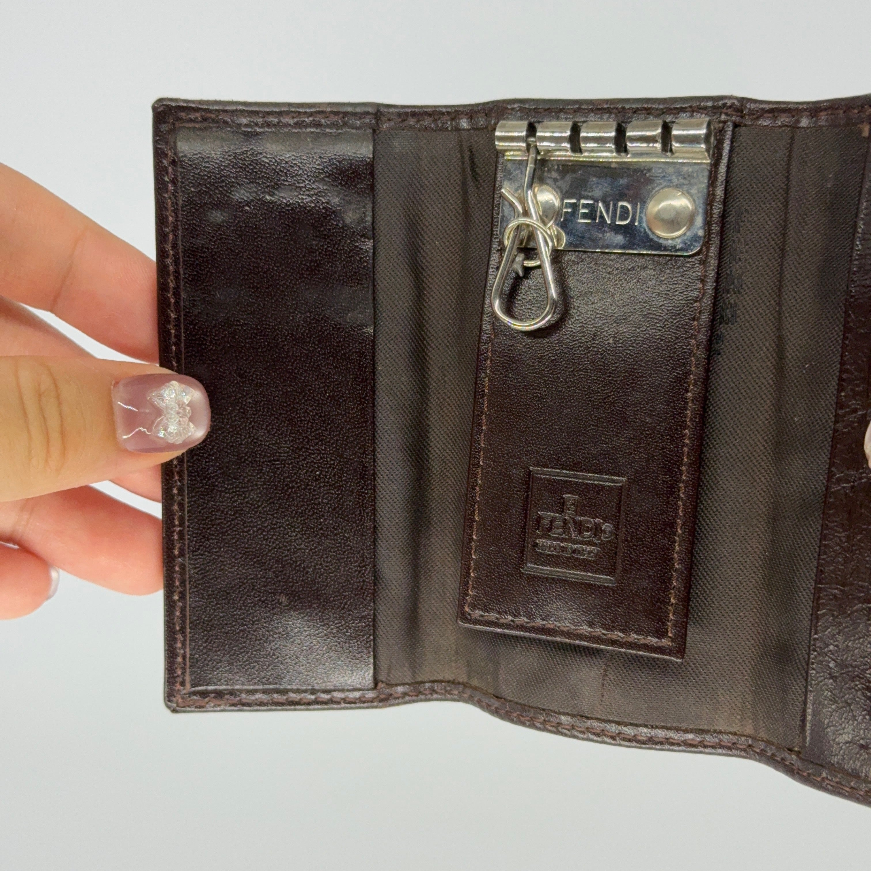 Fendi FF Zucca key case in brown canvas with dark brown leather trim and silver-tone hardware displayed closed against a white backdrop.