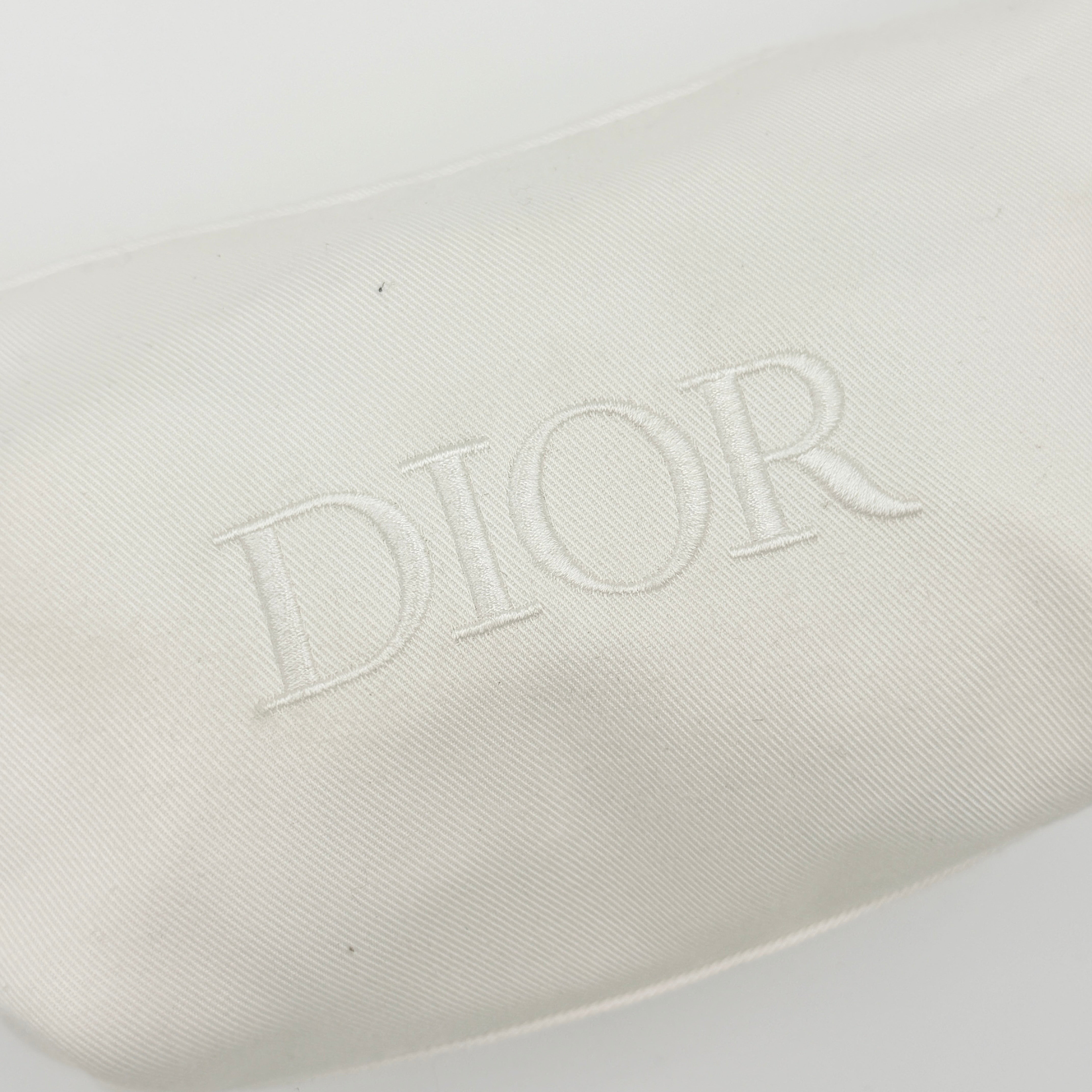 A structured white Dior pouch in twill with tonal logo embroidery and gold-tone zip, displayed against a pristine backdrop.