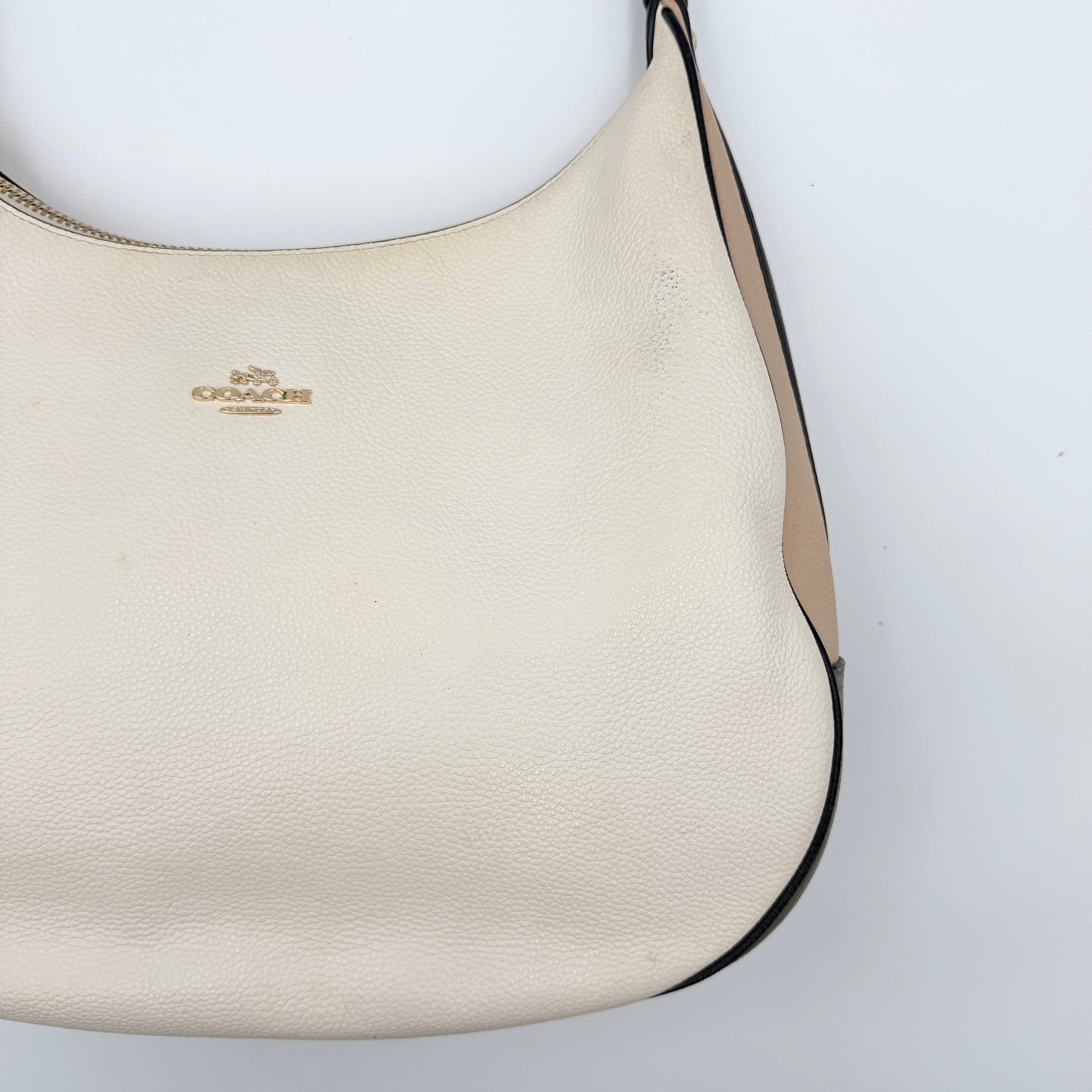 Coach Harley East West Hobo in cream and beige pebbled leather with a sculpted silhouette, black piping, and silver hardware.