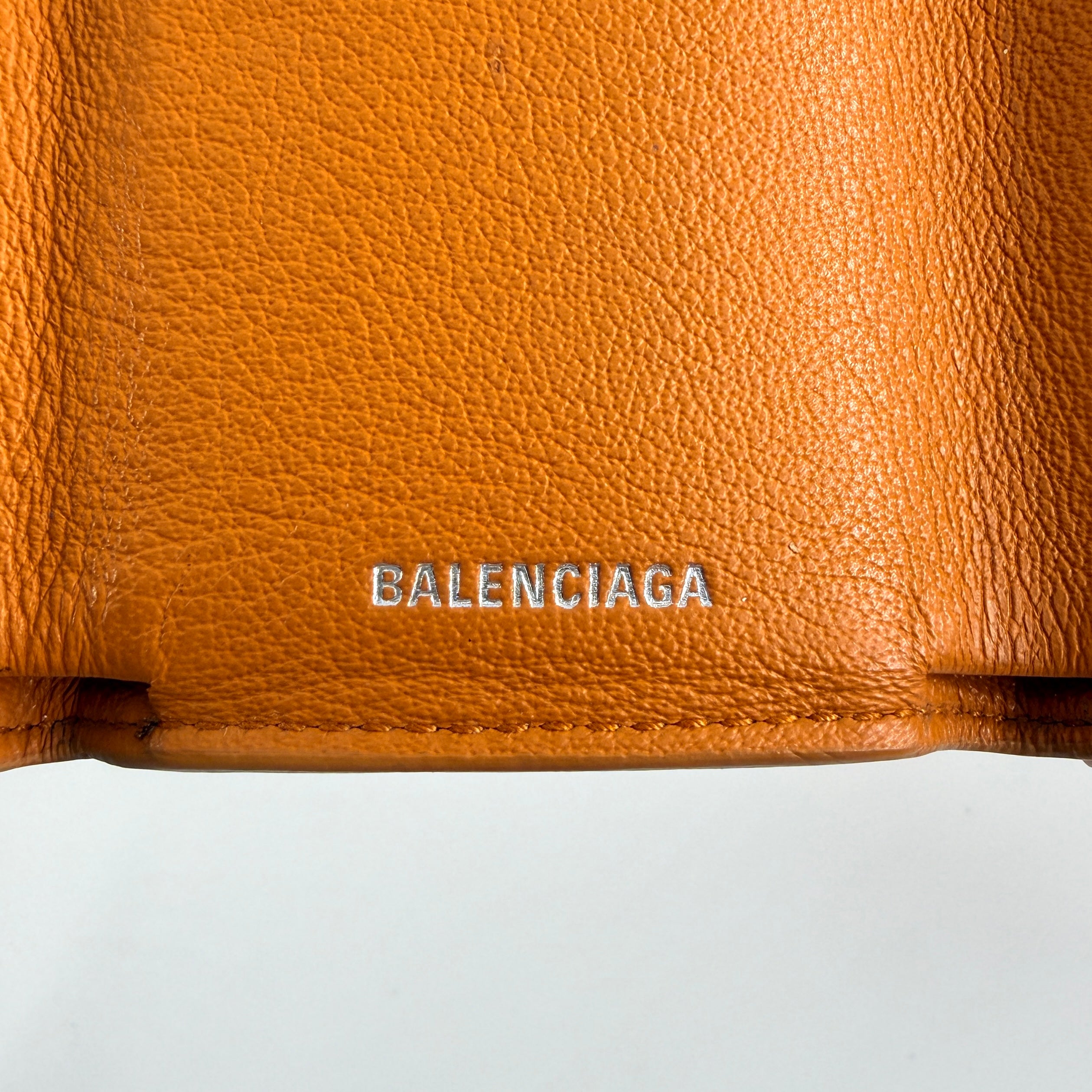 Balenciaga Papier Mini Wallet in vibrant orange grained leather, showcasing its envelope-style flap and silver logo detail.