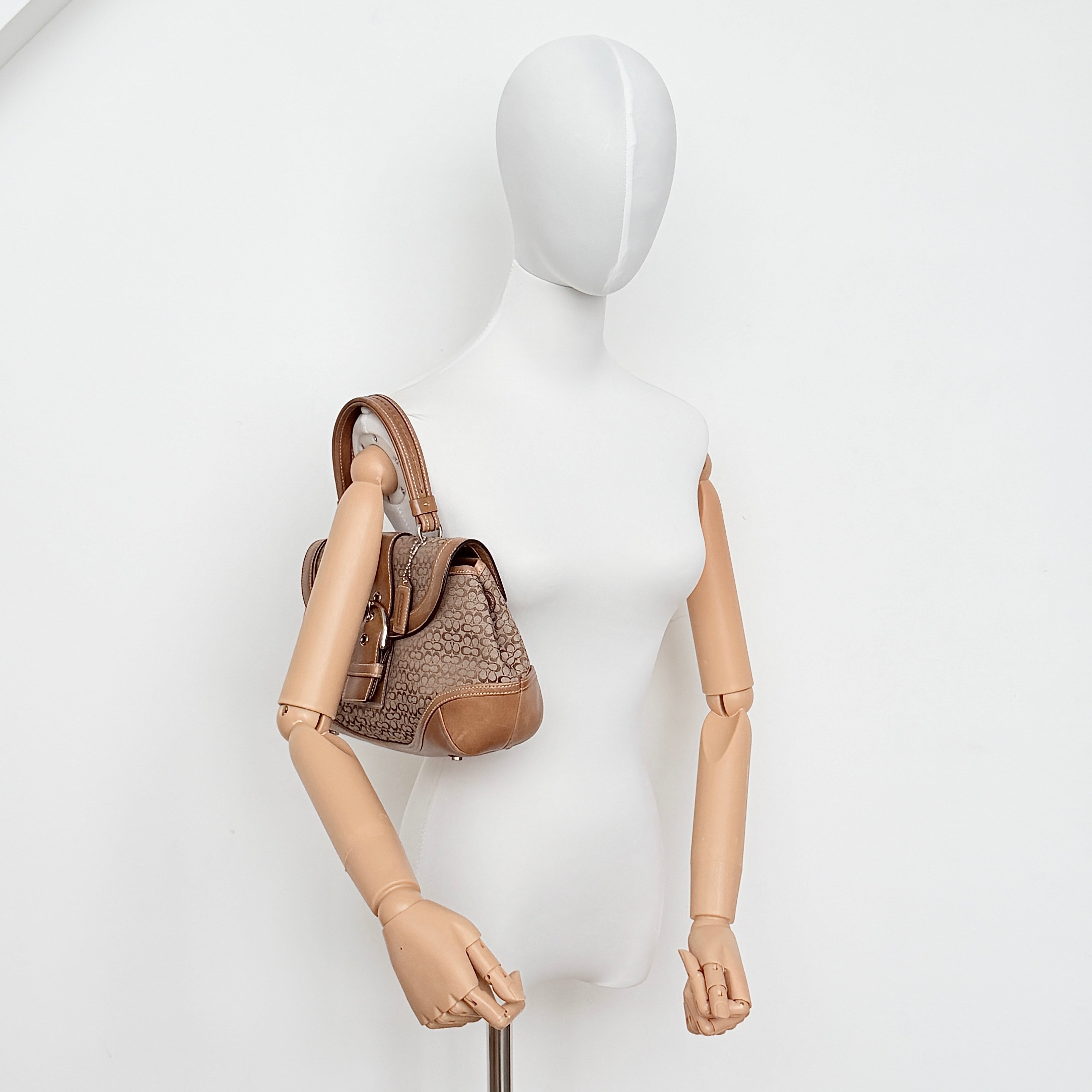 Coach Signature Soho shoulder bag in beige jacquard canvas with tan leather trim and silver buckle, shown against a white background.