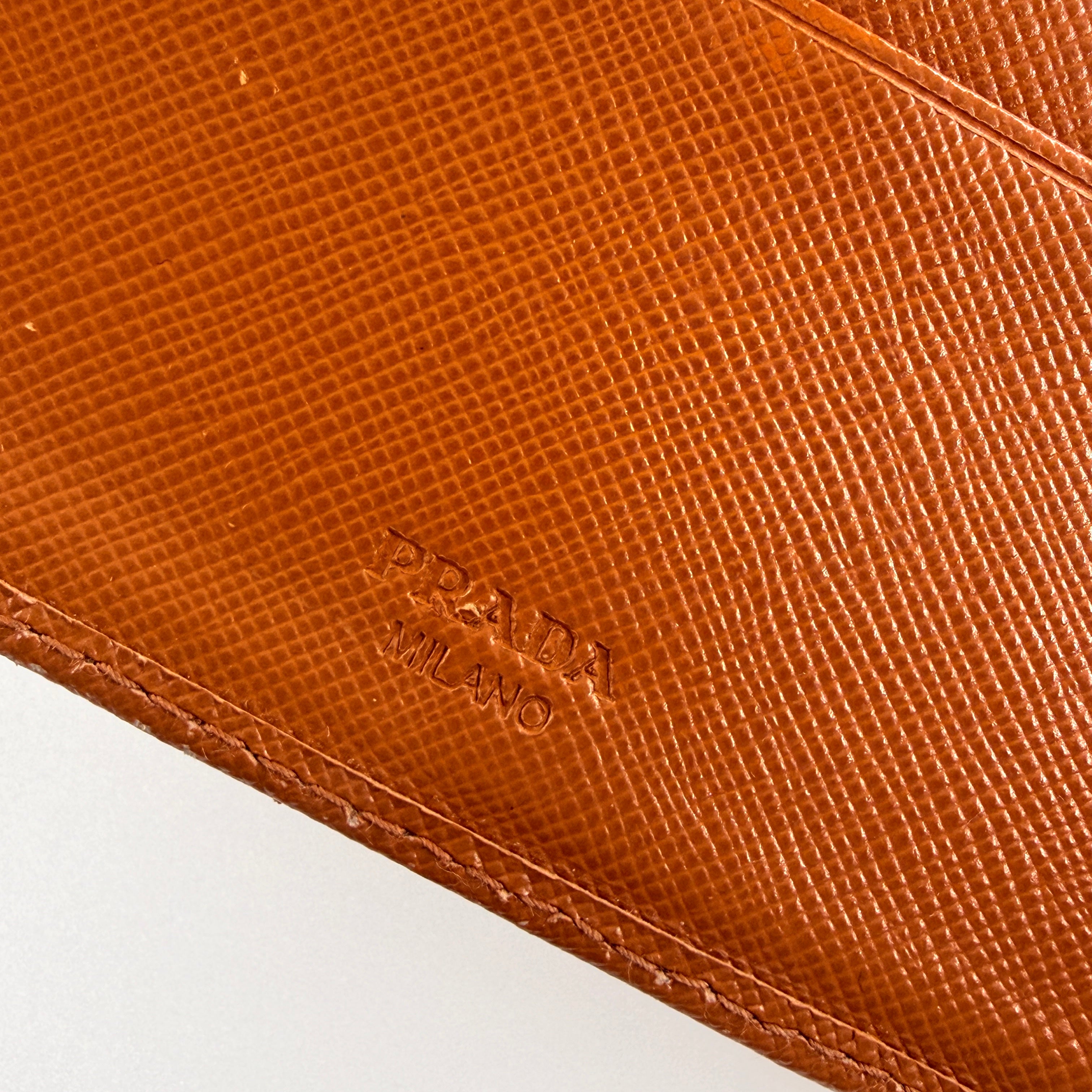 Prada Saffiano Leather Trifold Wallet in brown leather with gold-tone logo, showcasing its structured flap and crosshatch texture.