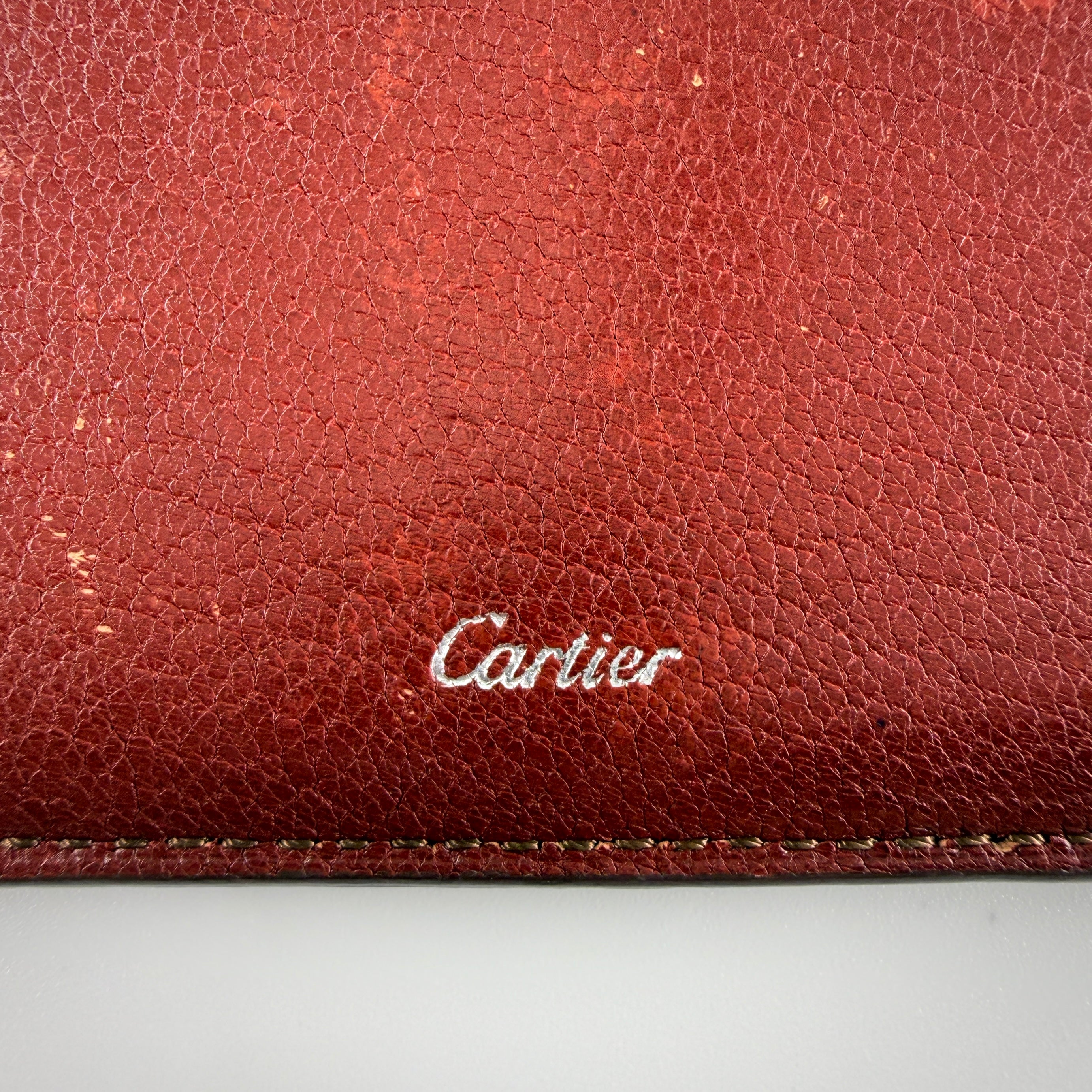 Must de Cartier burgundy leather cardholder with visible natural texture and Cartier script logo, photographed against a clean background.