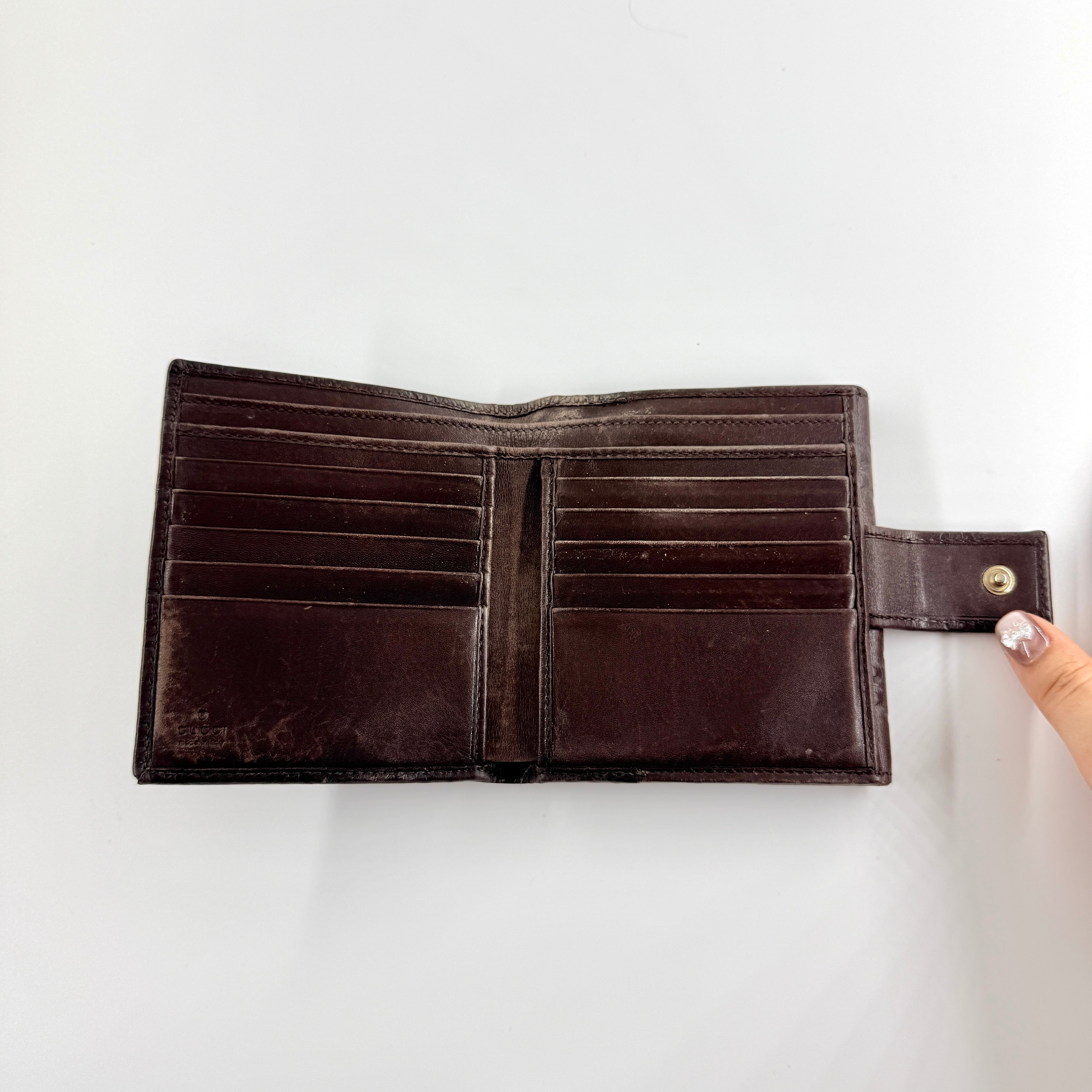 Front-facing Gucci GG Monogram Guccissima wallet in deep brown embossed leather with gold-tone bar accent.