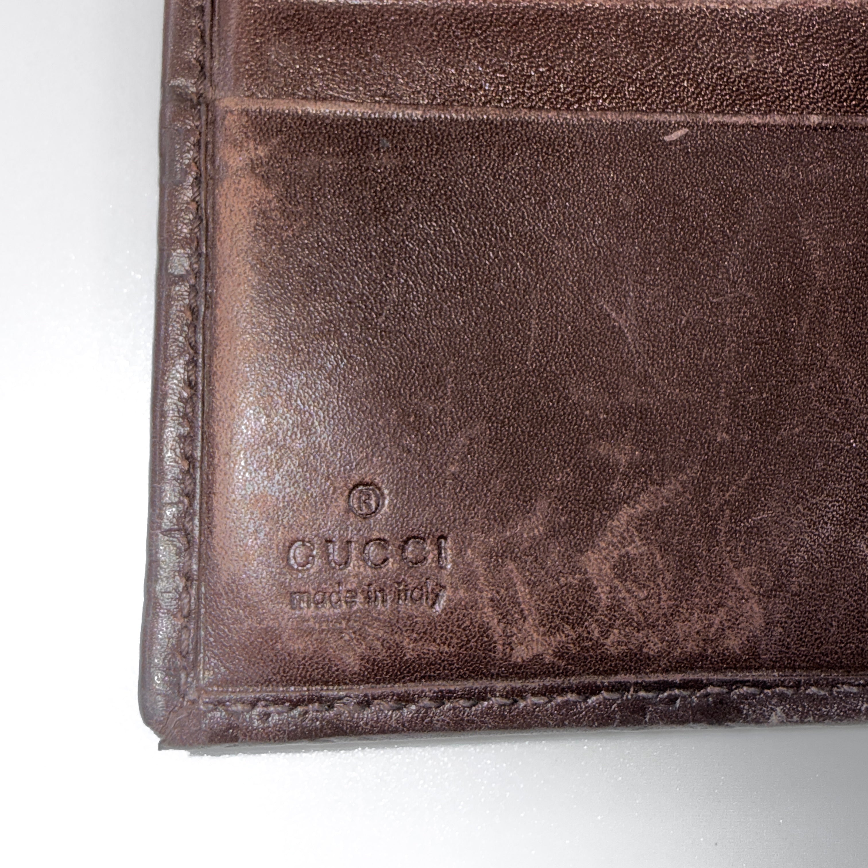Front-facing Gucci GG Monogram Guccissima wallet in deep brown embossed leather with gold-tone bar accent.
