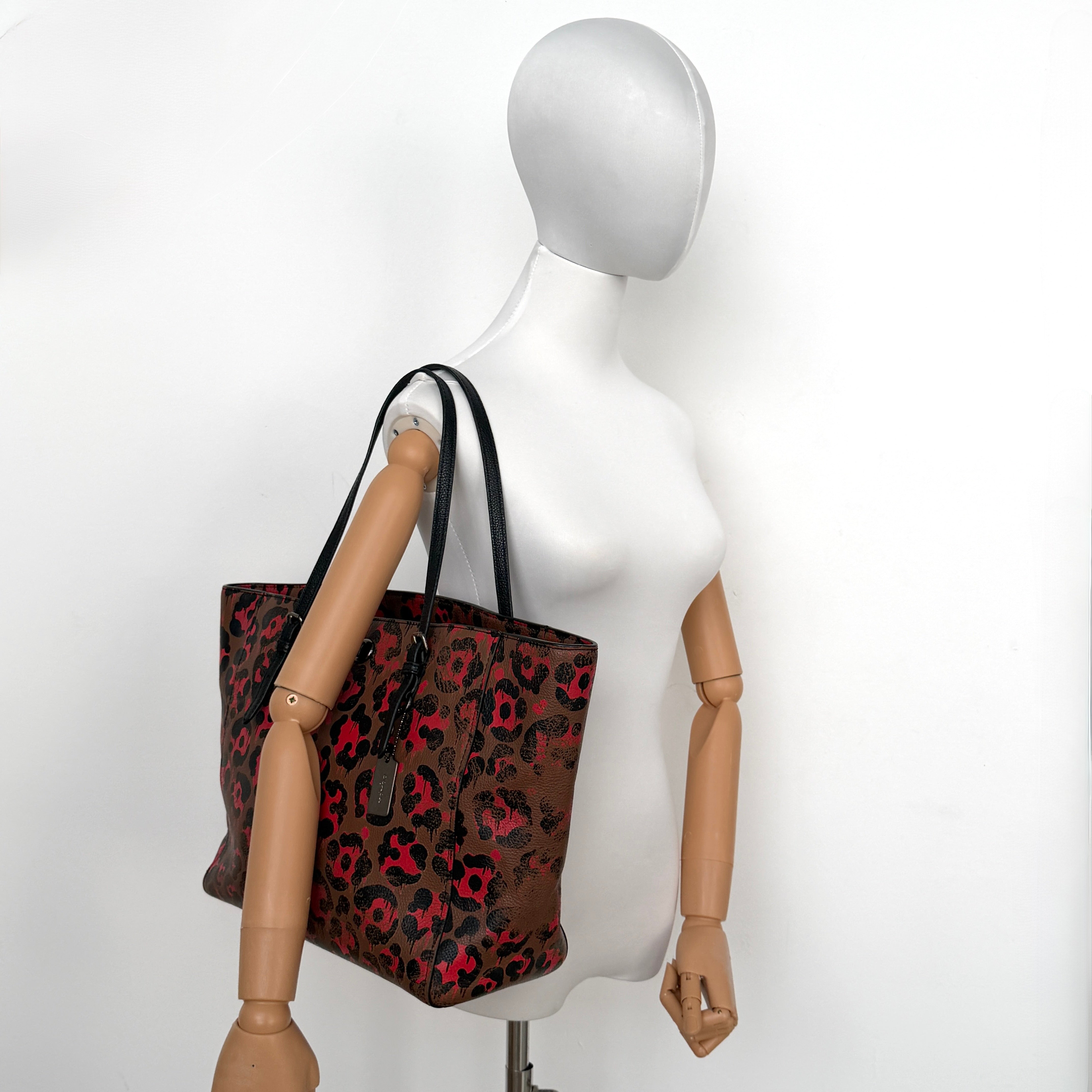 Coach City Tote in brown coated canvas, drenched in a vivid red and black leopard print, with black leather handles and silver hardware details.