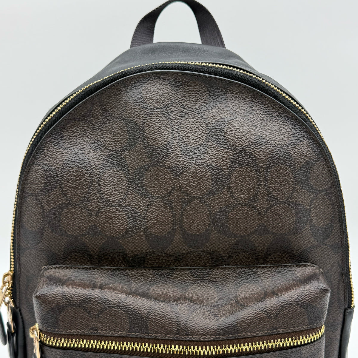 Coach Signature Charlie Backpack in brown and black canvas with gold-tone hardware and front zip pocket.