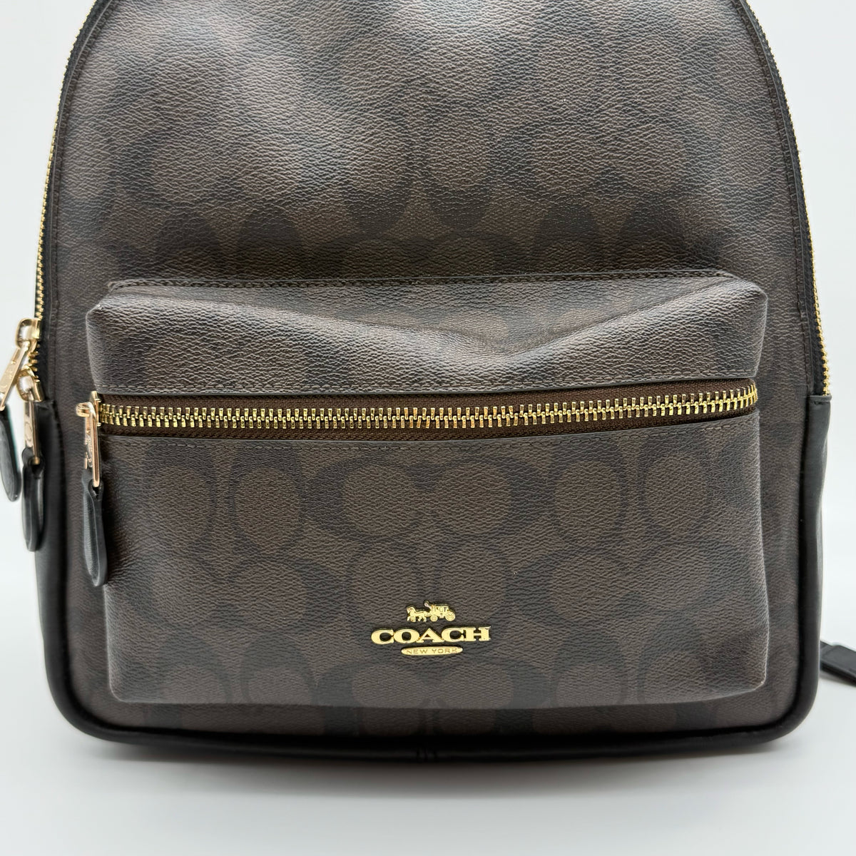Coach Signature Charlie Backpack in brown and black canvas with gold-tone hardware and front zip pocket.