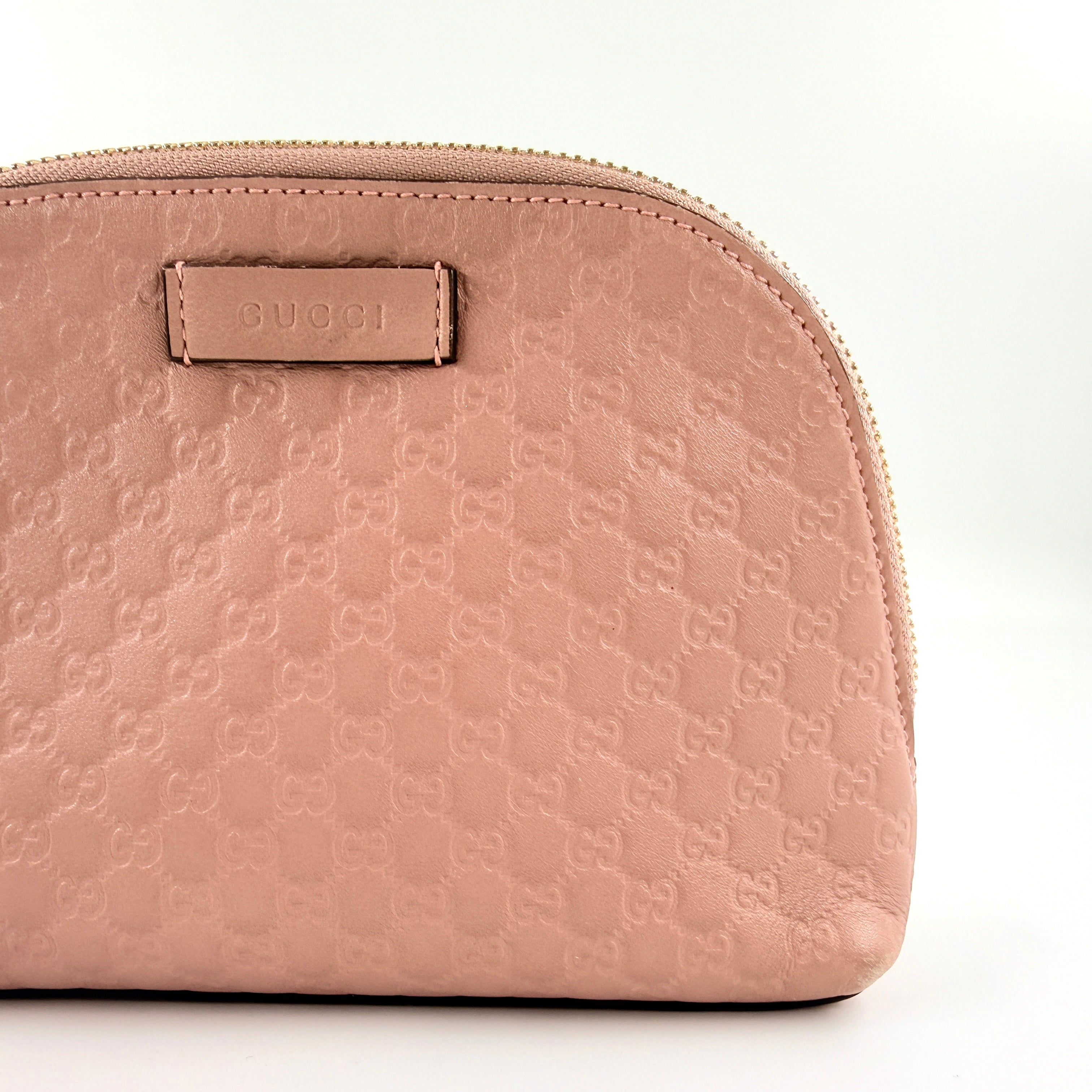 Gucci GG Monogram Guccissima cosmetic pouch in blush pink leather with signature embossed motif and gold-tone zip hardware.